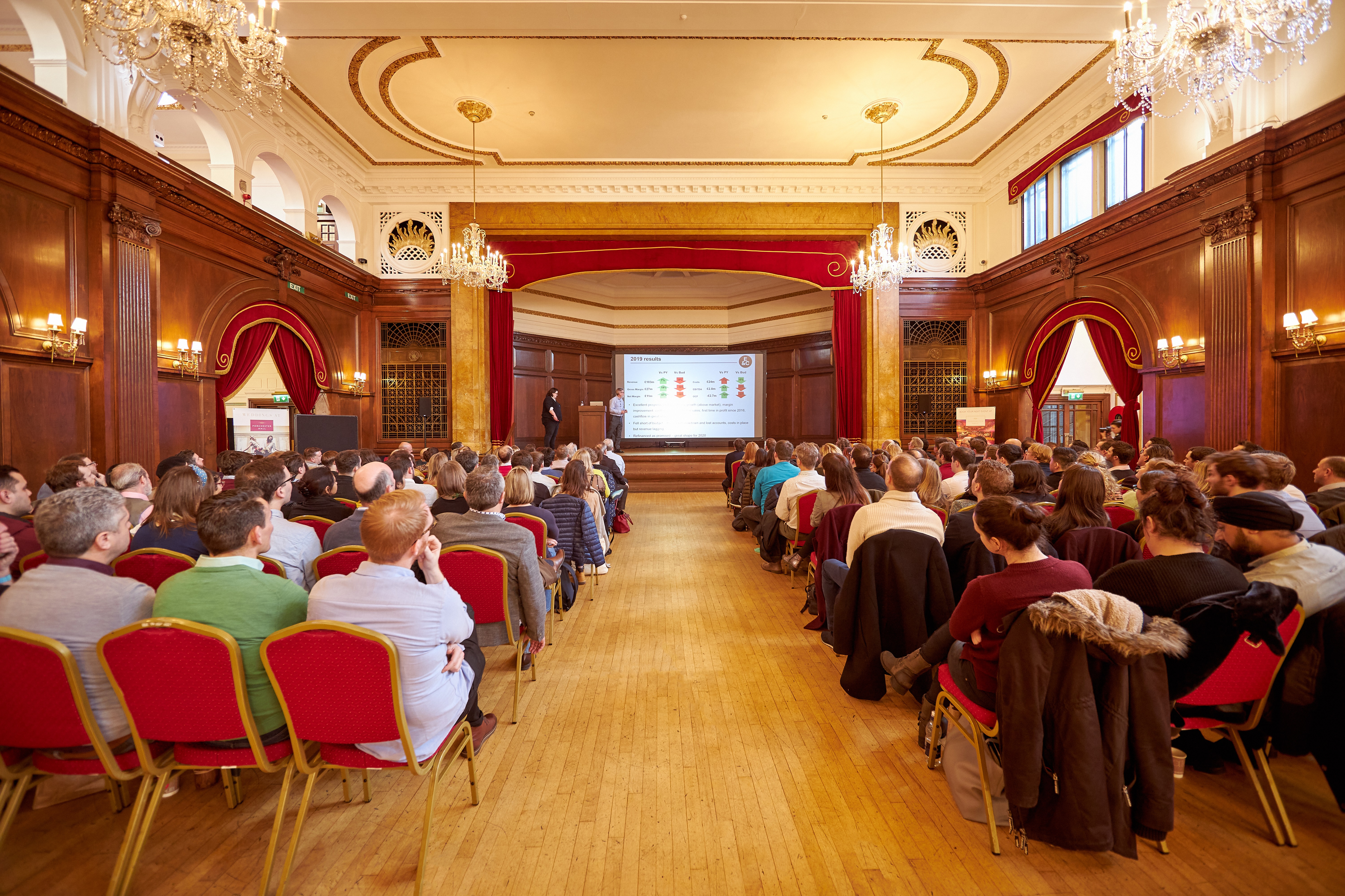 Elegant Porchester Hall conference with red chairs and warm wood paneling.