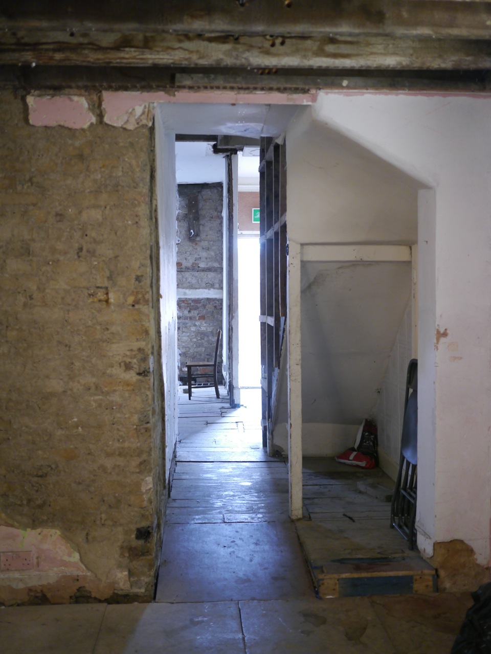 Narrow corridor with rustic walls leading to bright exit, perfect for events and branding.