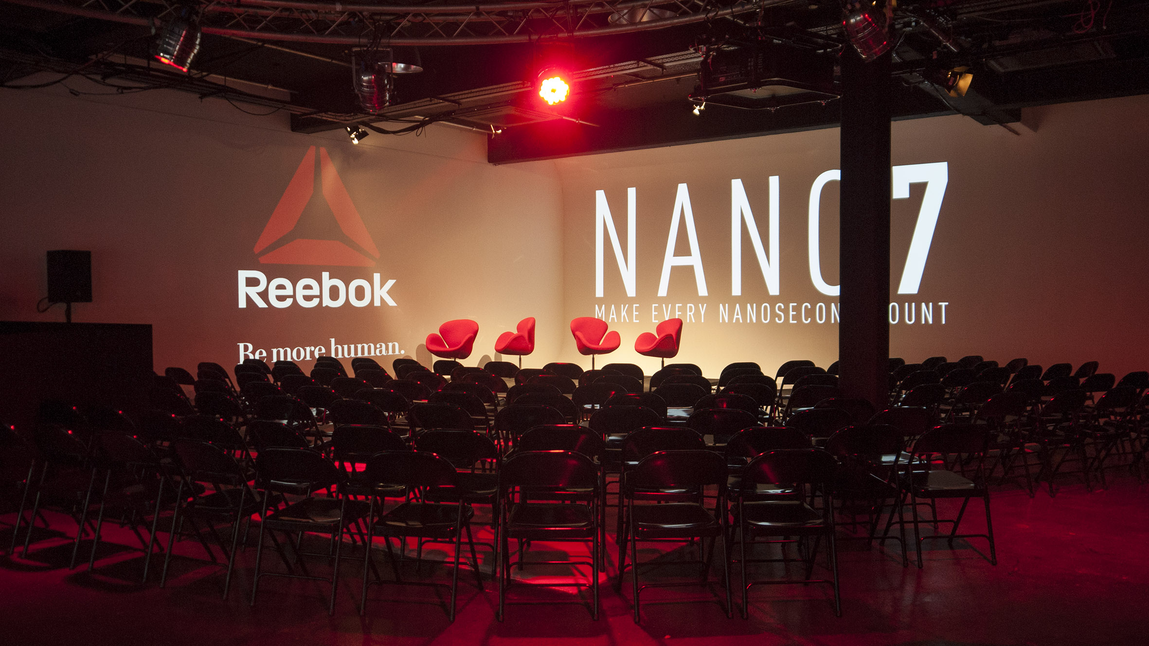 Event space with Reebok backdrop, red lighting for panel discussion or presentation.