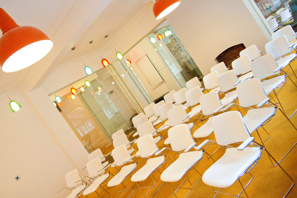 Modern meeting room with white chairs and colorful pendant lights for workshops and presentations.