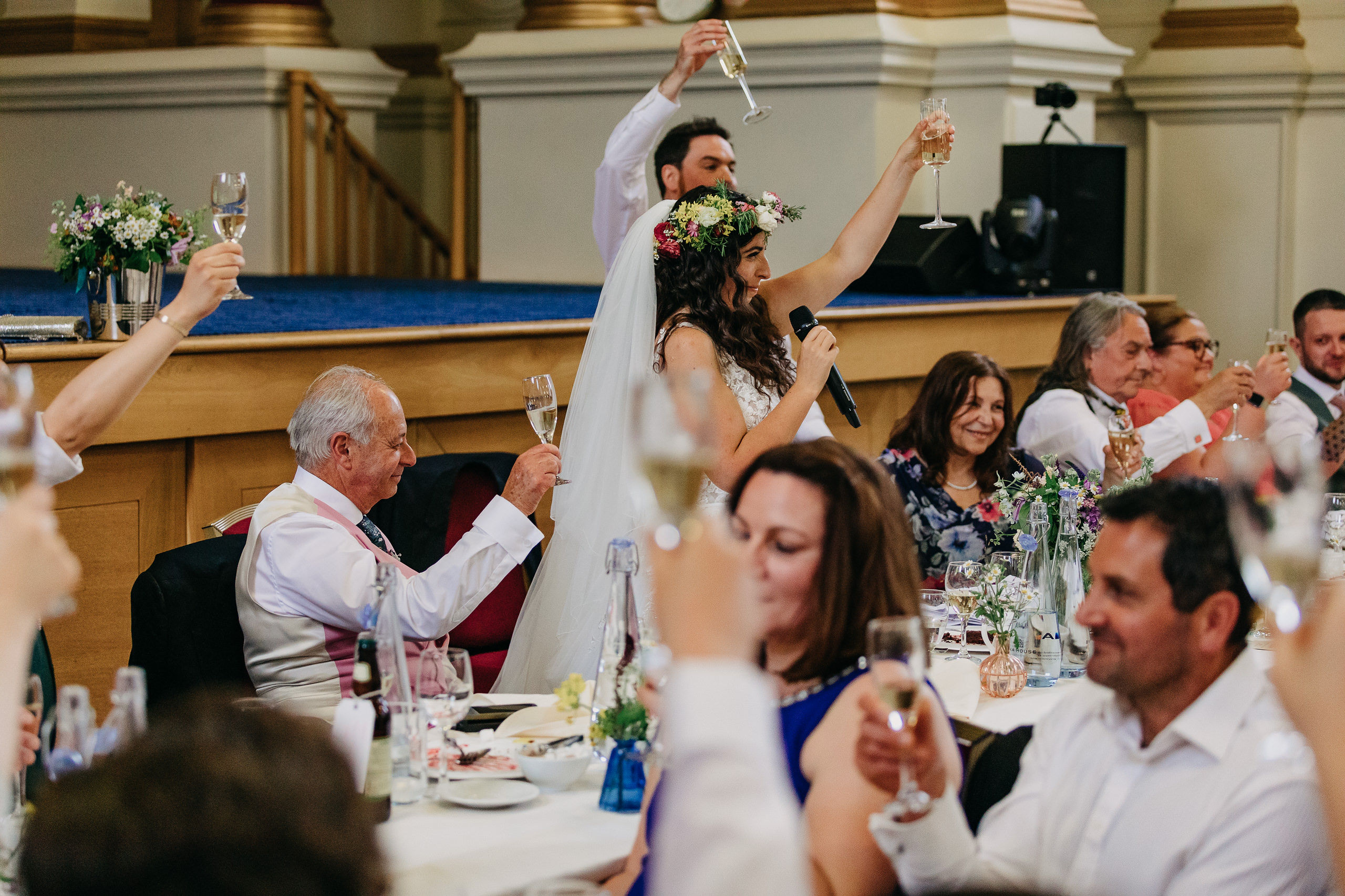 Wedding reception in Great Hall, BMA House; bride with floral crown toasts guests.
