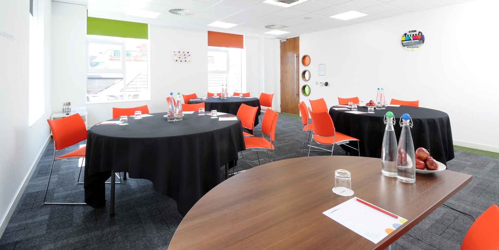 Modern meeting room at Evolve Manchester with round tables and vibrant orange chairs.