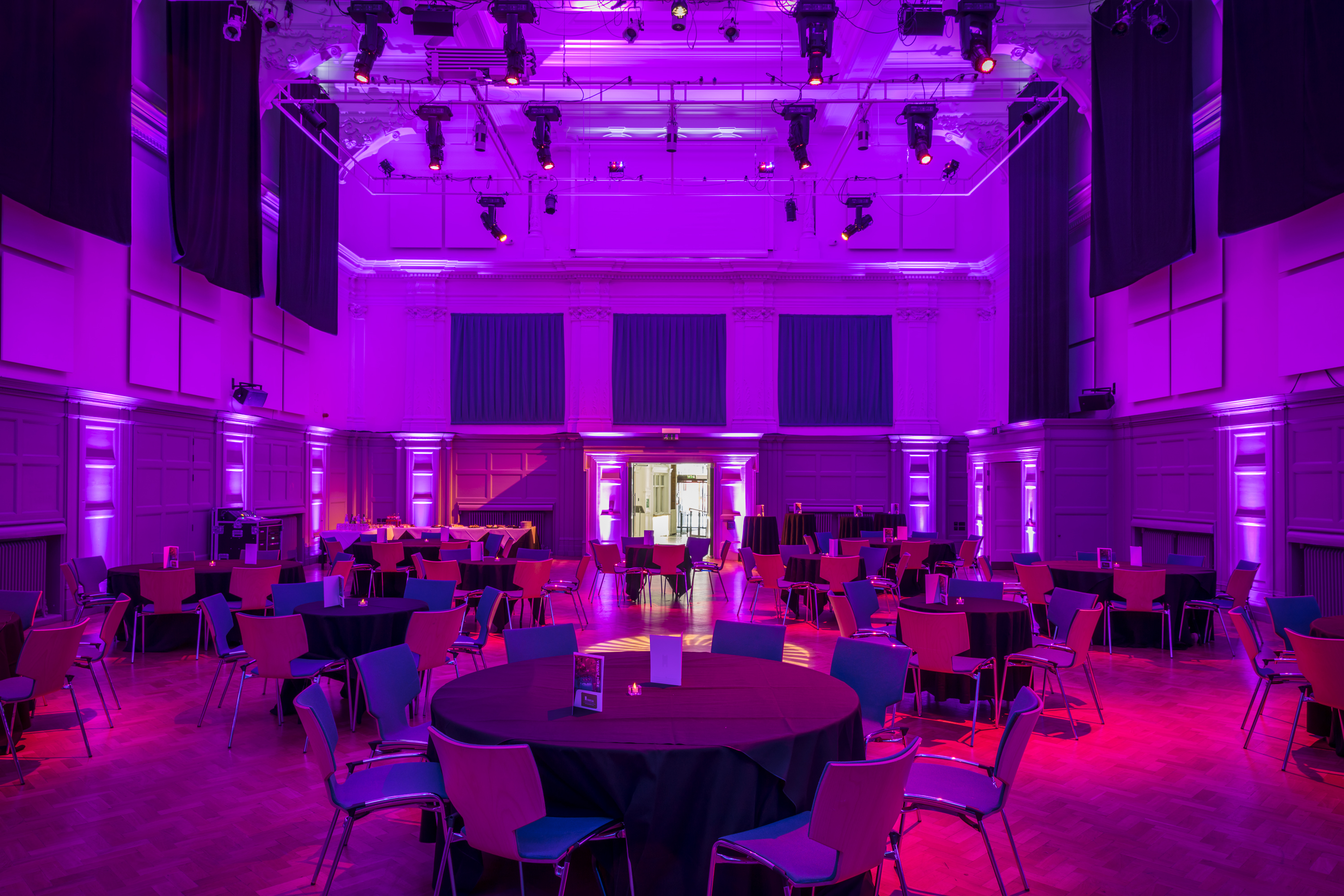 Great Hall at Bishopsgate Institute with round tables and vibrant purple lighting for events.