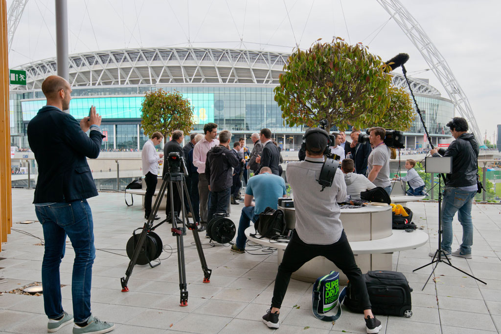 Outdoor event setup at Wembley Stadium with professionals discussing media coverage.