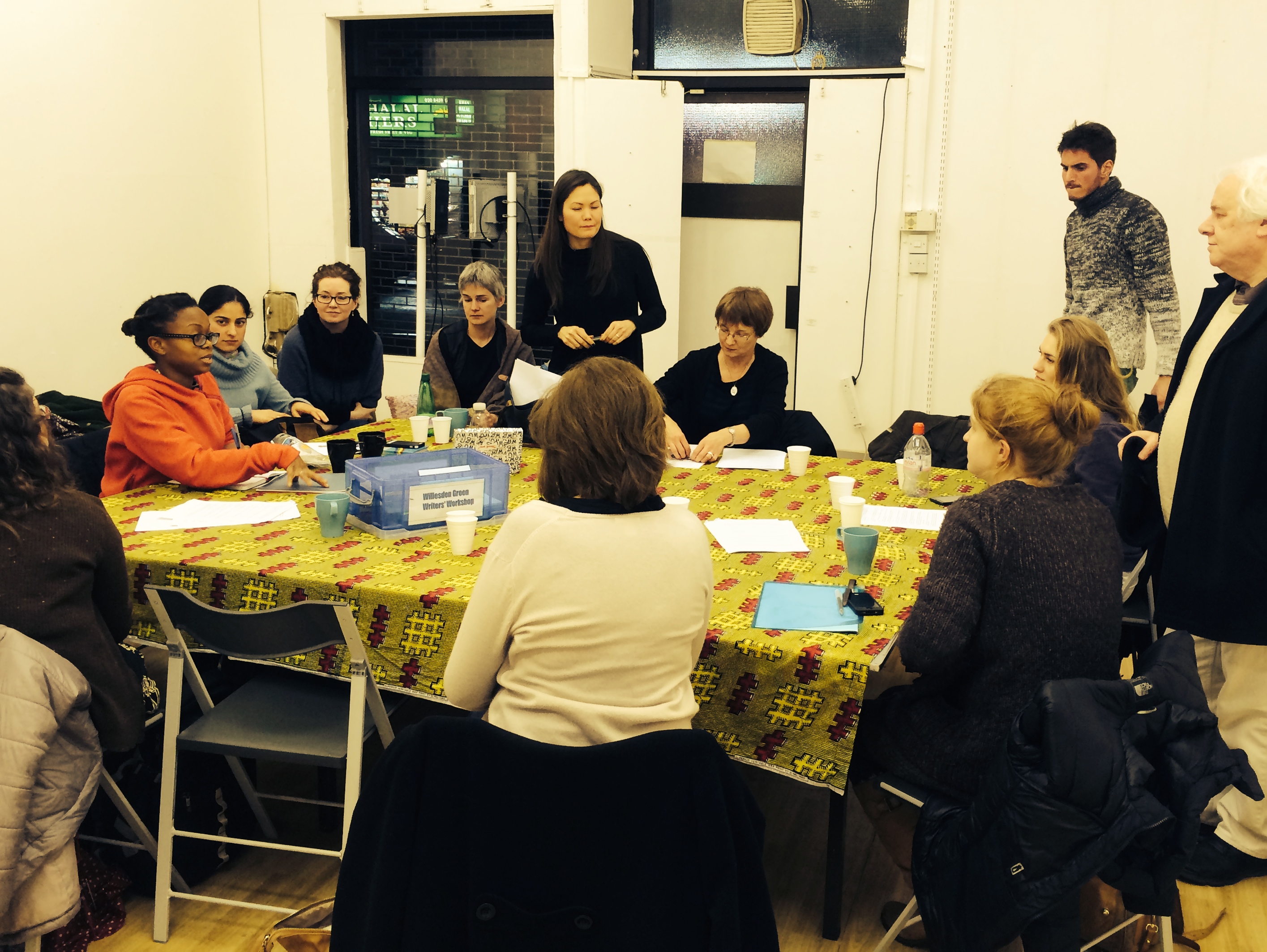 Diverse group collaborating at BAR Gallery, vibrant tablecloth enhances teamwork atmosphere.