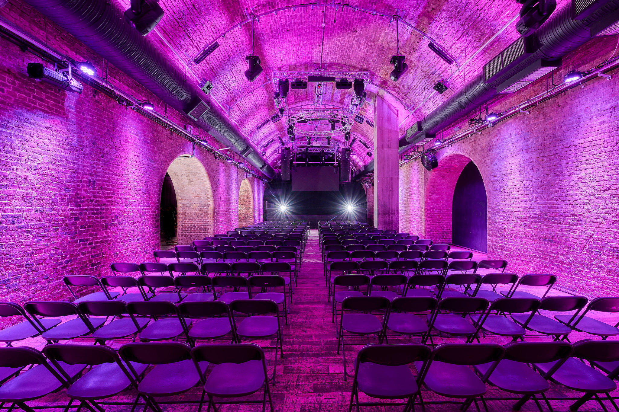 Stylish arched brick venue with purple lighting for conferences and performances.
