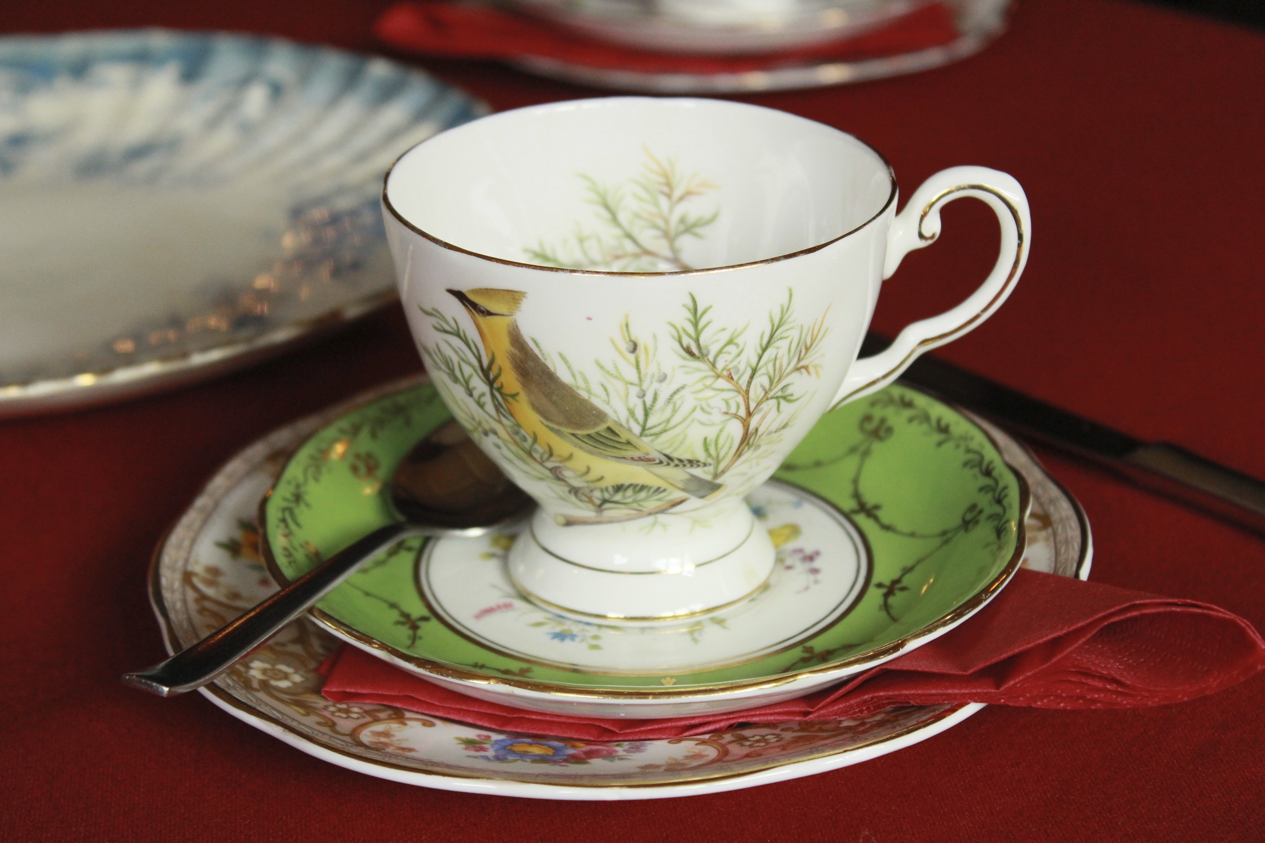 Elegant tea setup with bird motif china on red tablecloth for formal high tea.