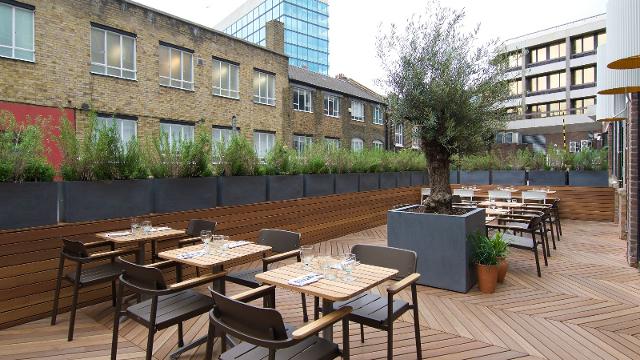Outdoor event space with wooden furniture and greenery for networking and alfresco dining.