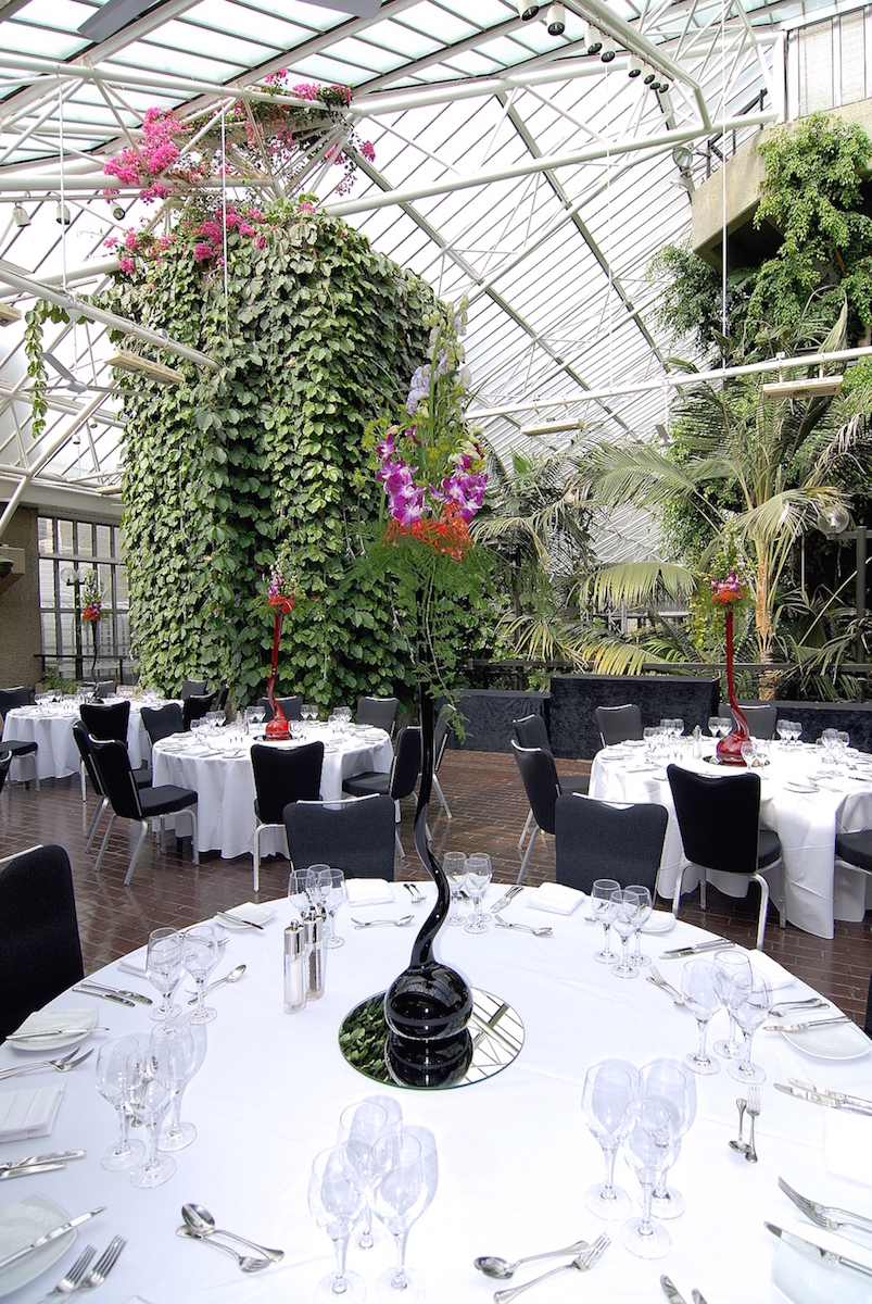 Elegant event space at Barbican Centre with lush greenery and floral centerpieces.