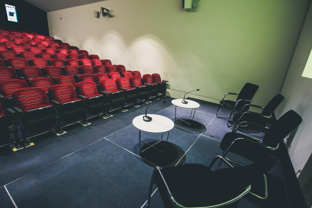 Cubic Theatre event space with panel setup, chairs, and microphones for presentations.