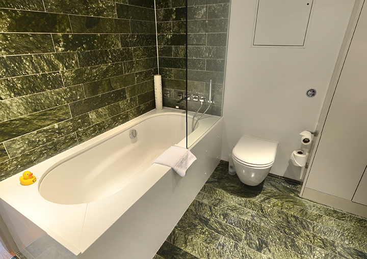 Modern Town Hall Hotel bathroom with sleek bathtub and green stone tiles for events.