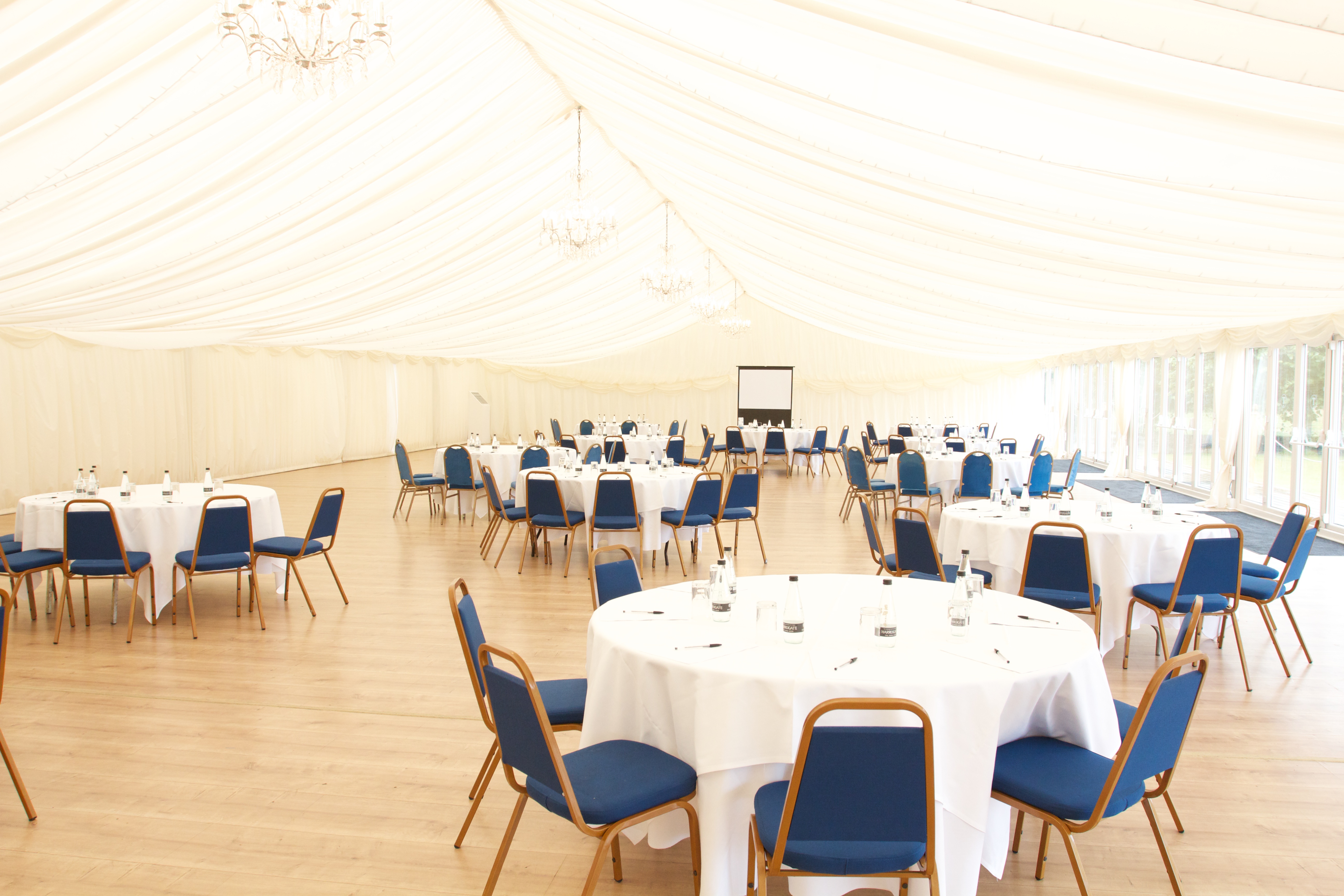 Spacious event tent at Quendon Hall with round tables for corporate meetings and banquets.