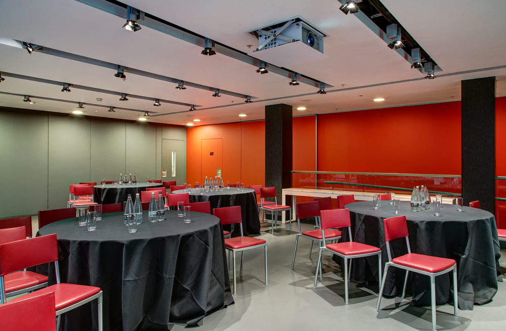 Modern meeting space in The Dorfman Room, featuring round tables and red chairs for events.