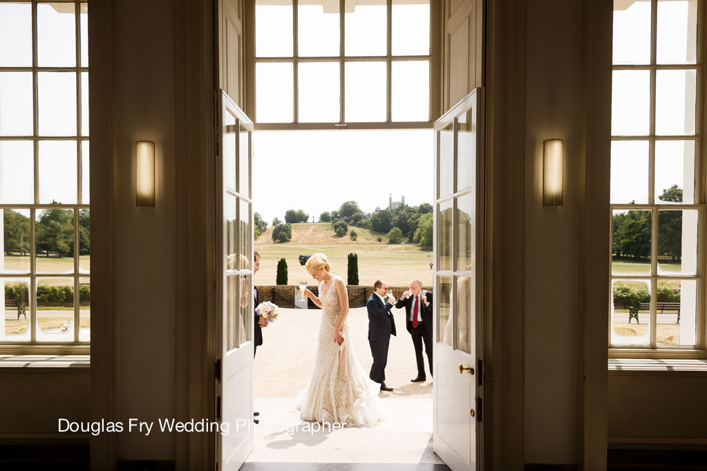 Bride at The Queen's House wedding venue entrance with elegant doors and lush backdrop.