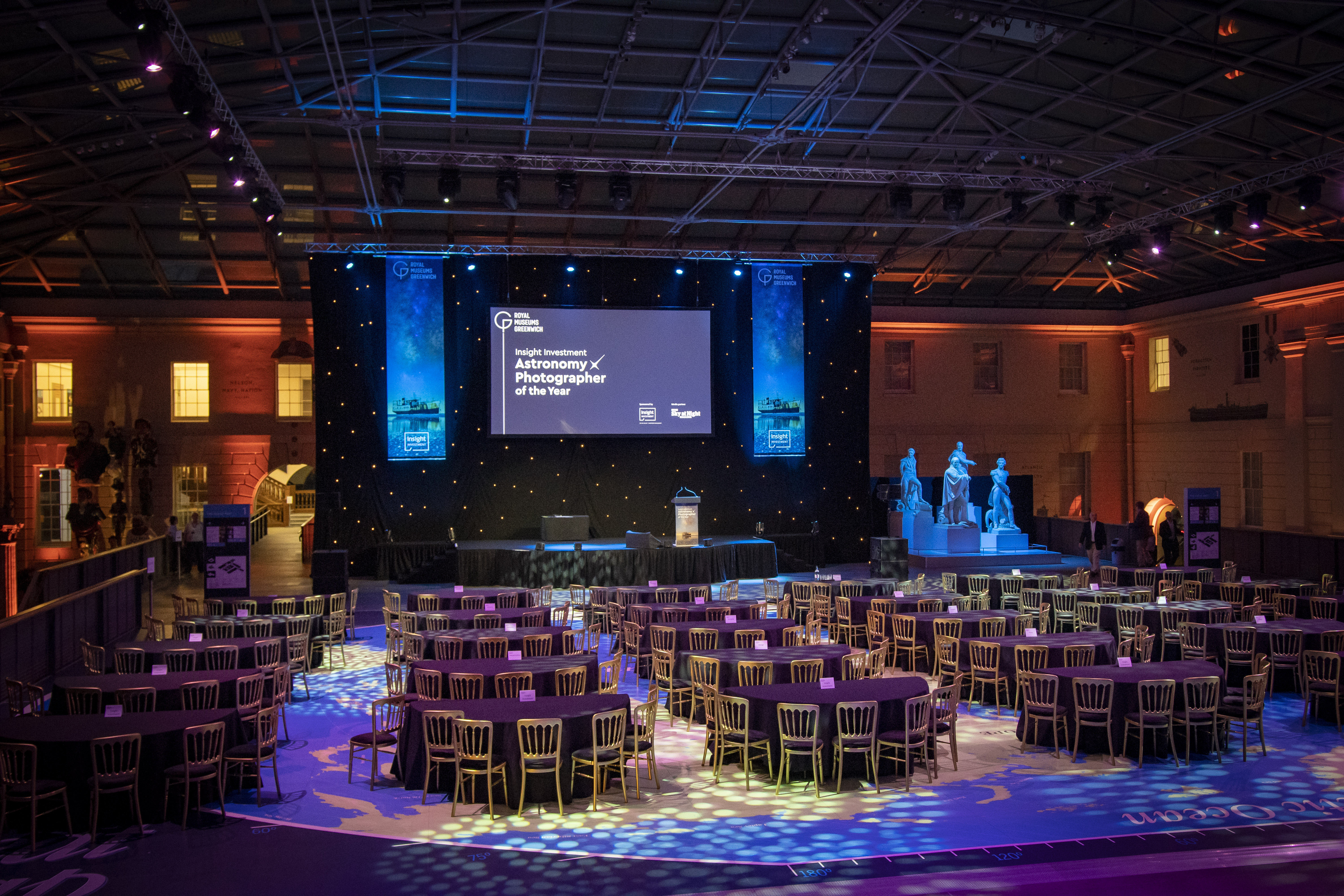 Elegant event space at National Maritime Museum with round tables and dynamic stage lighting.