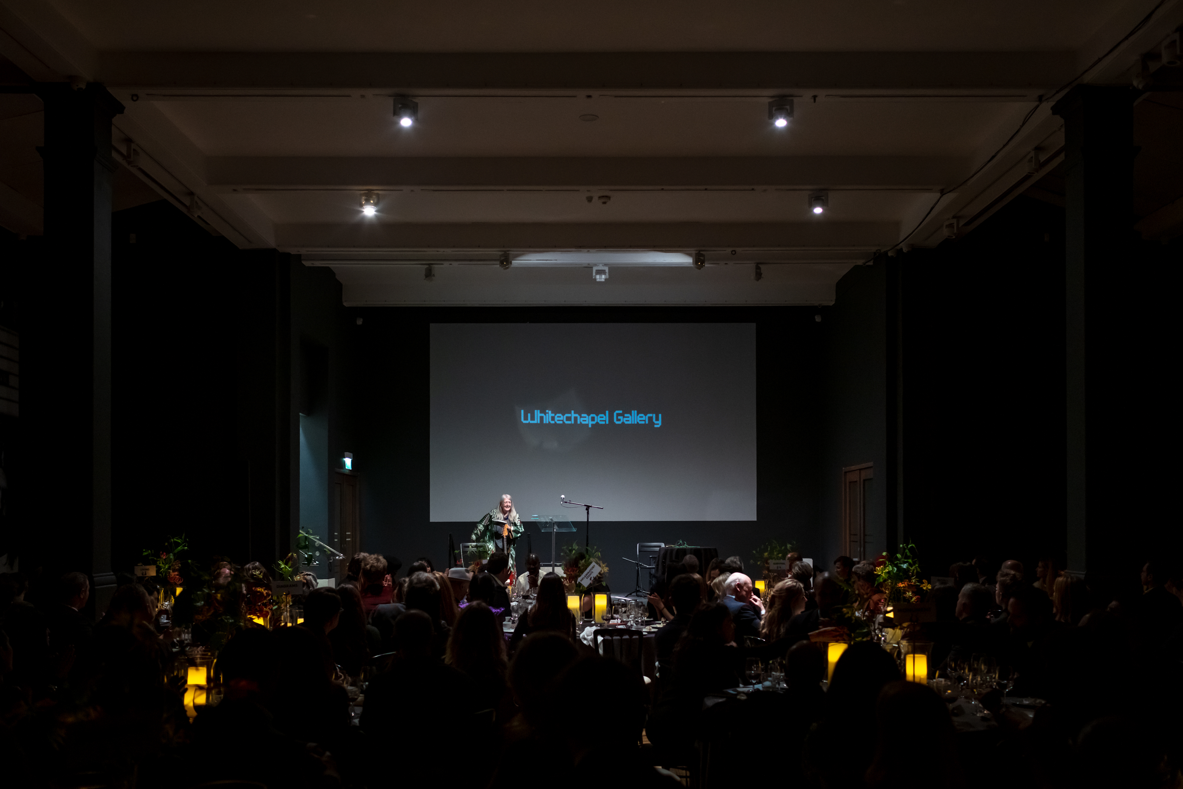 "Elegant event in Whitechapel Gallery with engaged audience and candlelit tables."