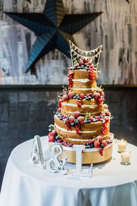 Multi-tiered wedding cake with berries and greenery at Balfour St Bart's venue.