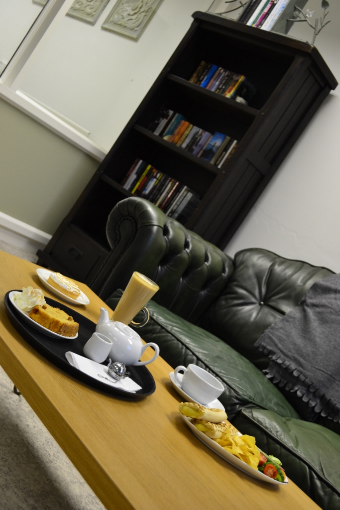 Cozy meeting space with green leather sofa, tea set, and pastries for creative discussions.