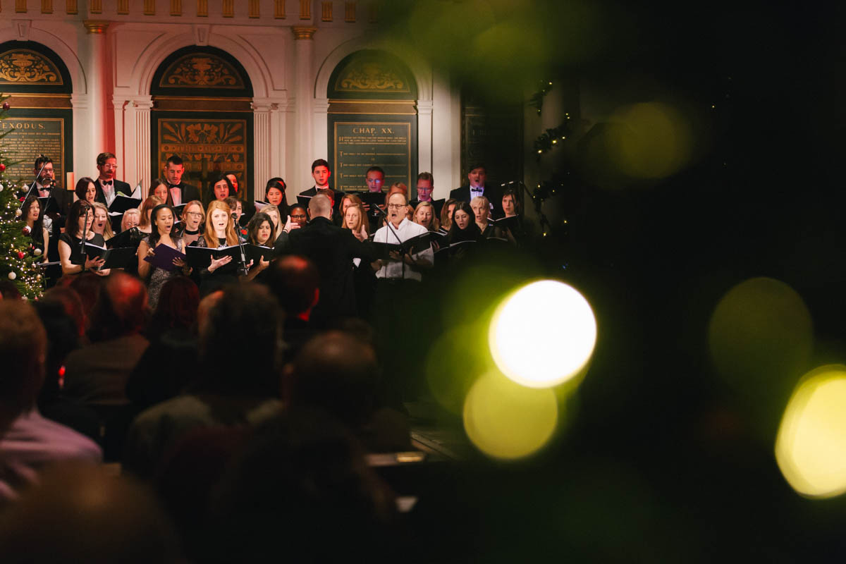 Choir performance in The Church in The Crypt, warm lighting, holiday event ambiance.