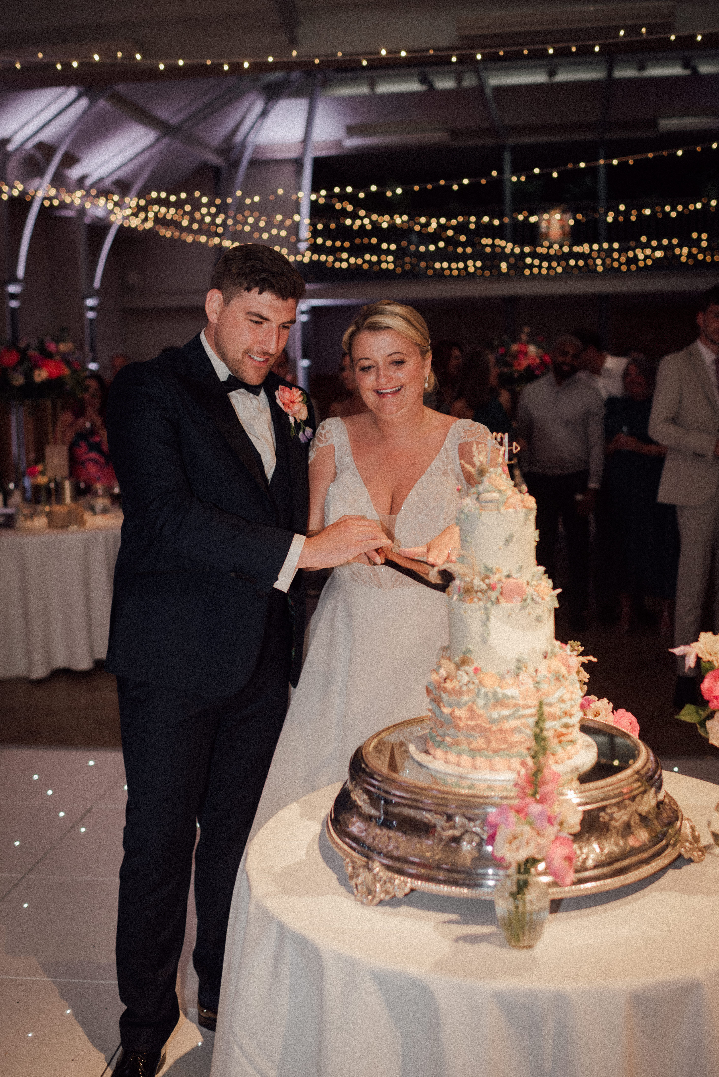 Couple cutting wedding cake in elegant HAC venue with fairy lights, perfect for celebrations.