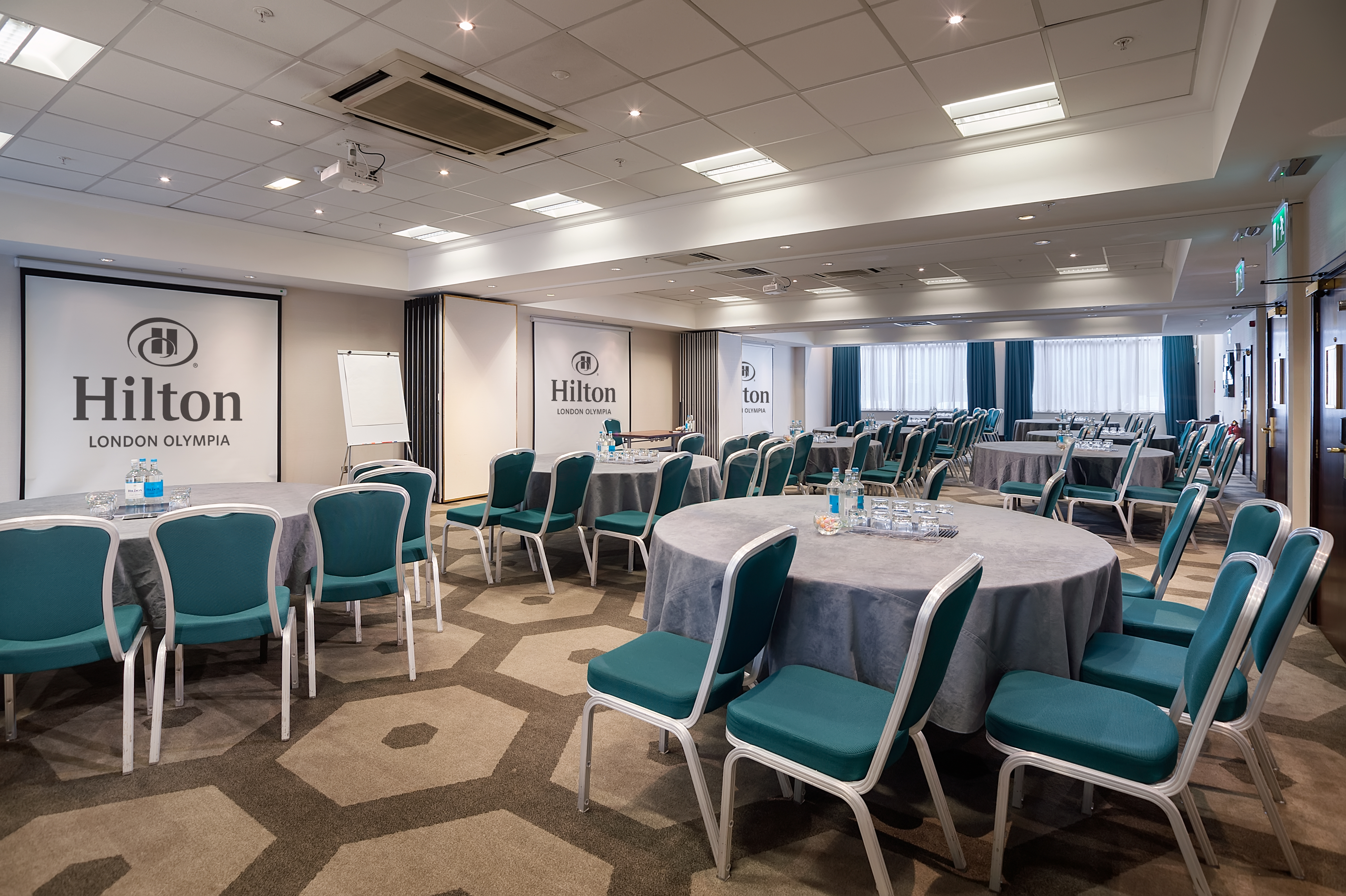 Pembroke Suite at Hilton London Olympia, featuring round tables and teal chairs for corporate events.