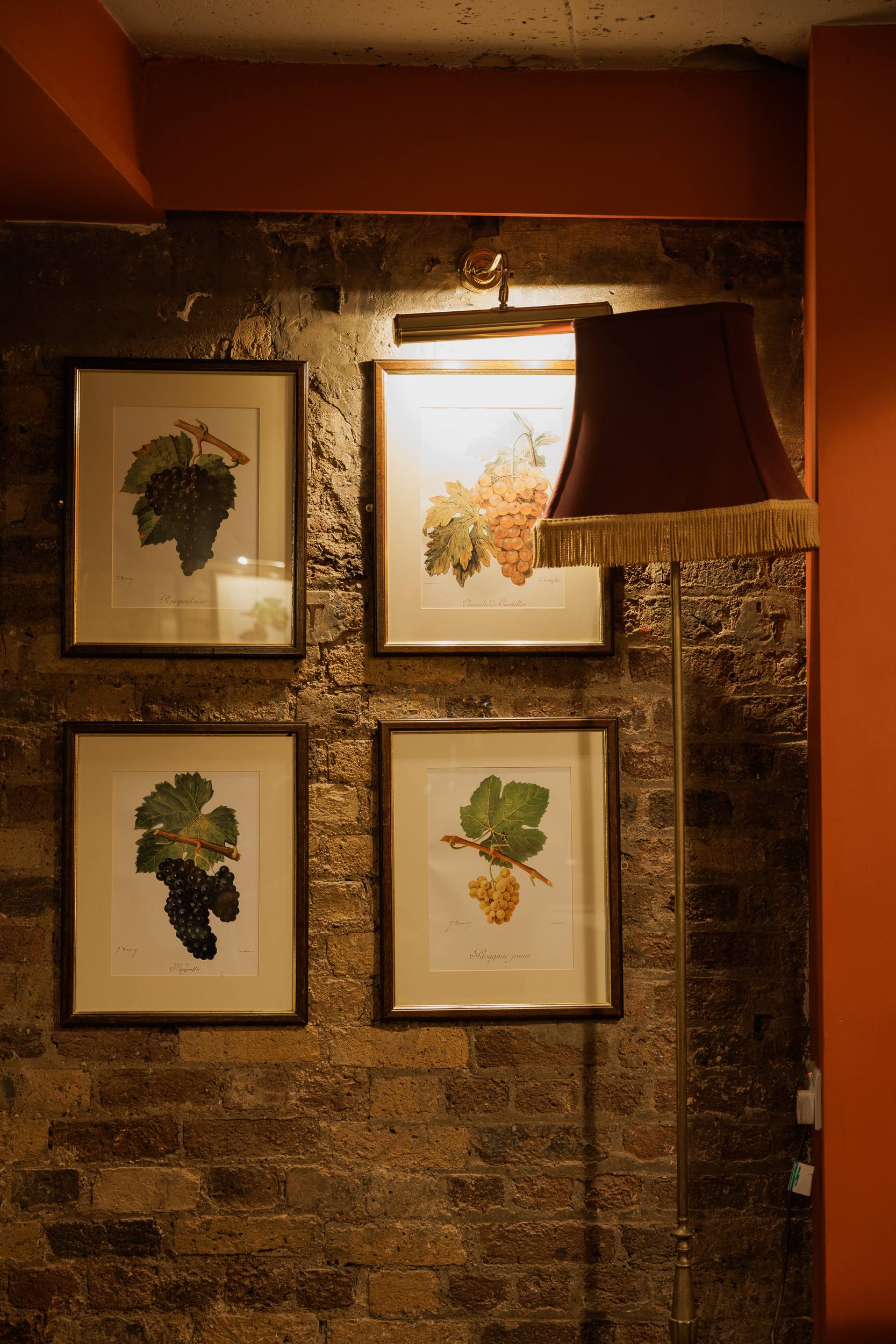 Wine cellar with framed grape illustrations, rustic brick wall, perfect for wine events.