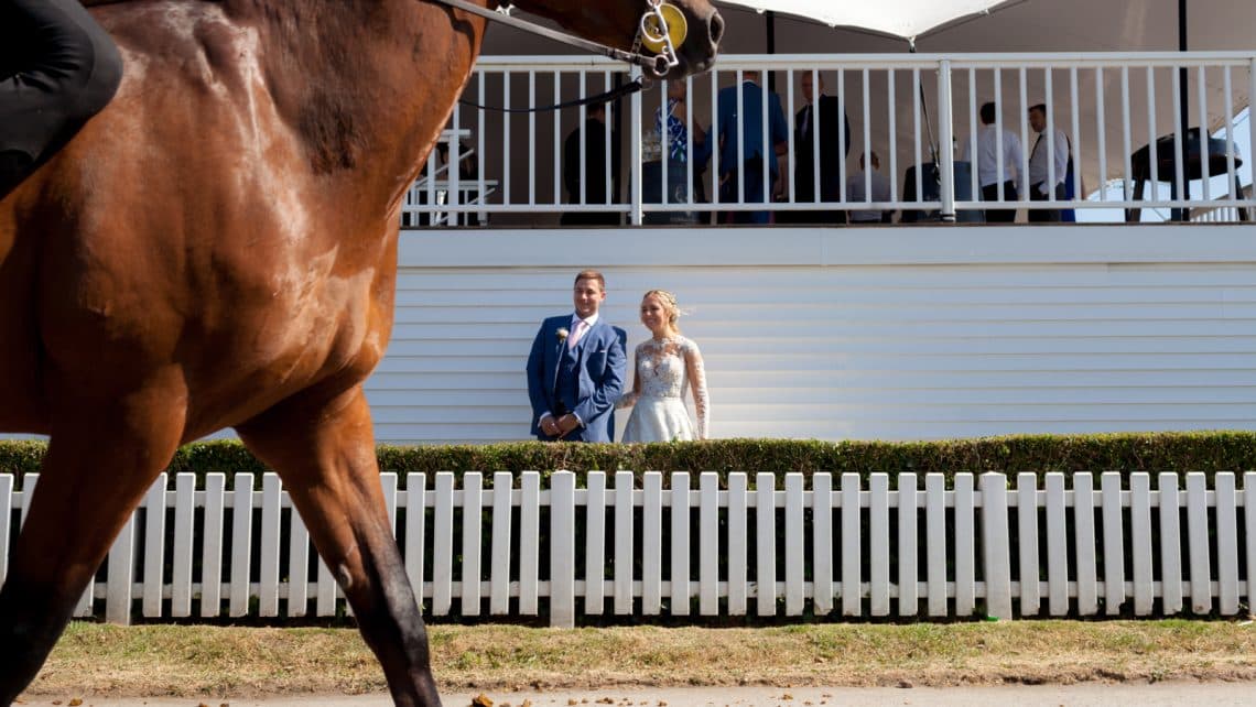 Outdoor wedding at Ham Polo Club with elegant couple and horse racing backdrop.