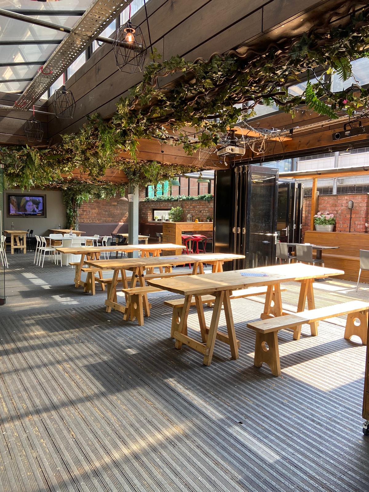 Versatile event space at The Greenhouse, featuring wooden tables and lush greenery.