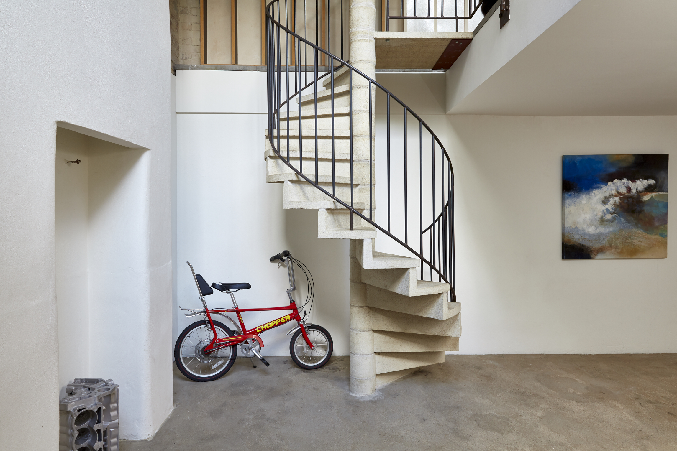 Modern minimalist venue with spiral staircase and red bicycle for creative events.