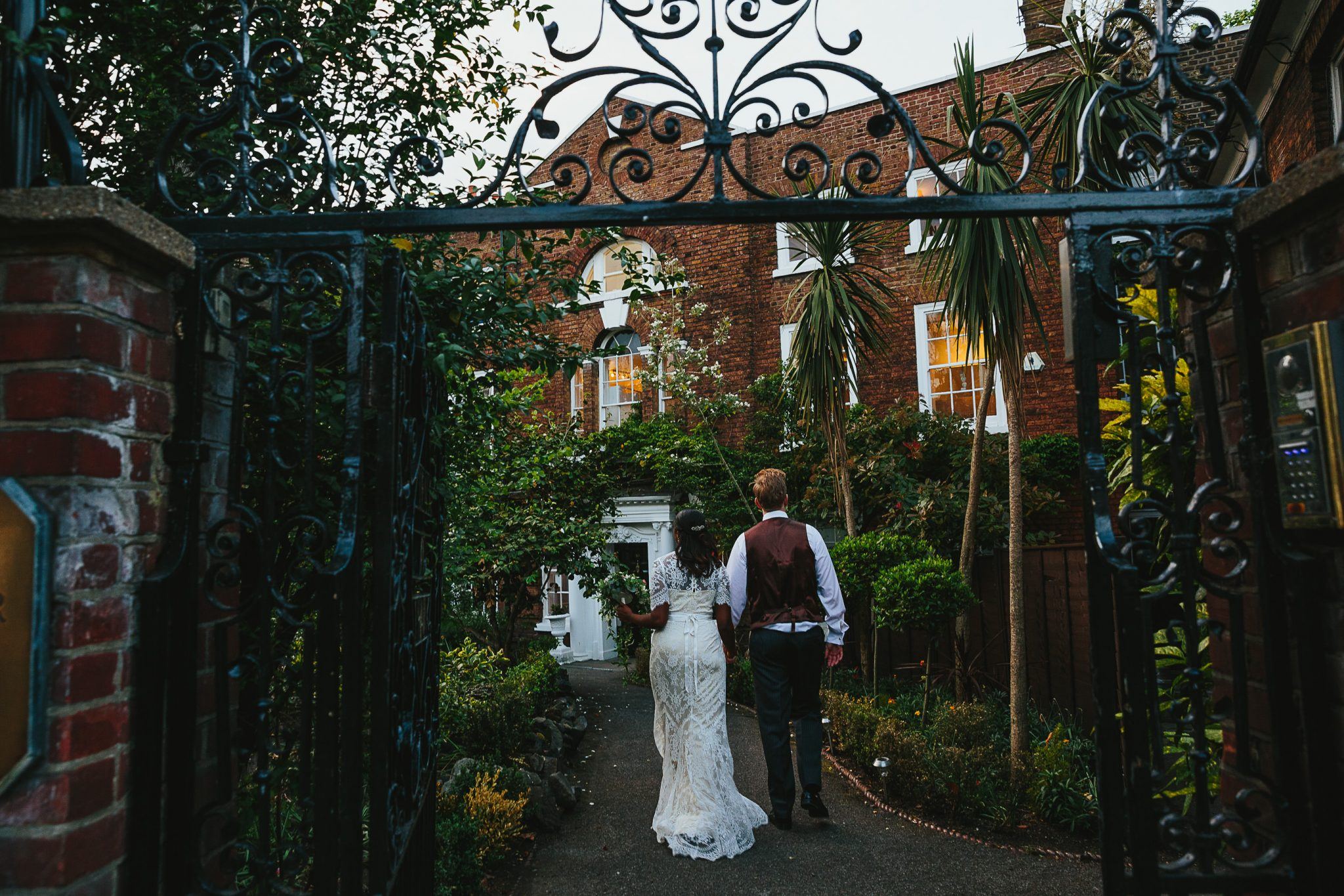Couple walking through ornate gate at romantic Winchester House event venue.