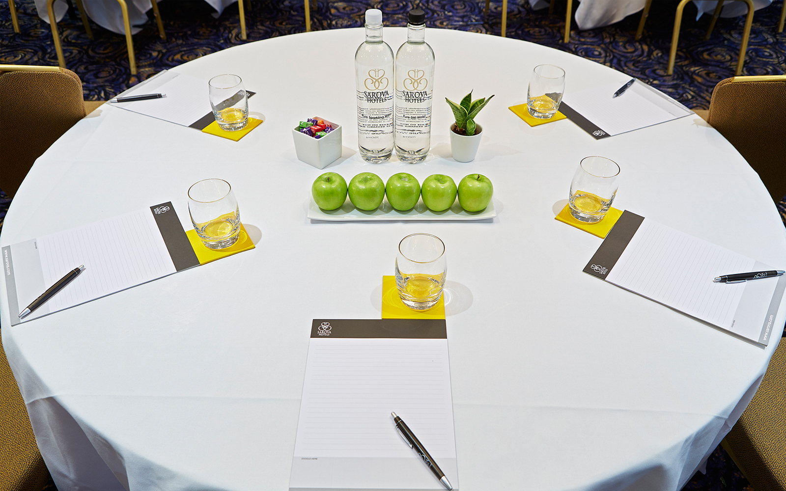 Queens Suite meeting setup with round table, notepads, and fresh decor for corporate events.