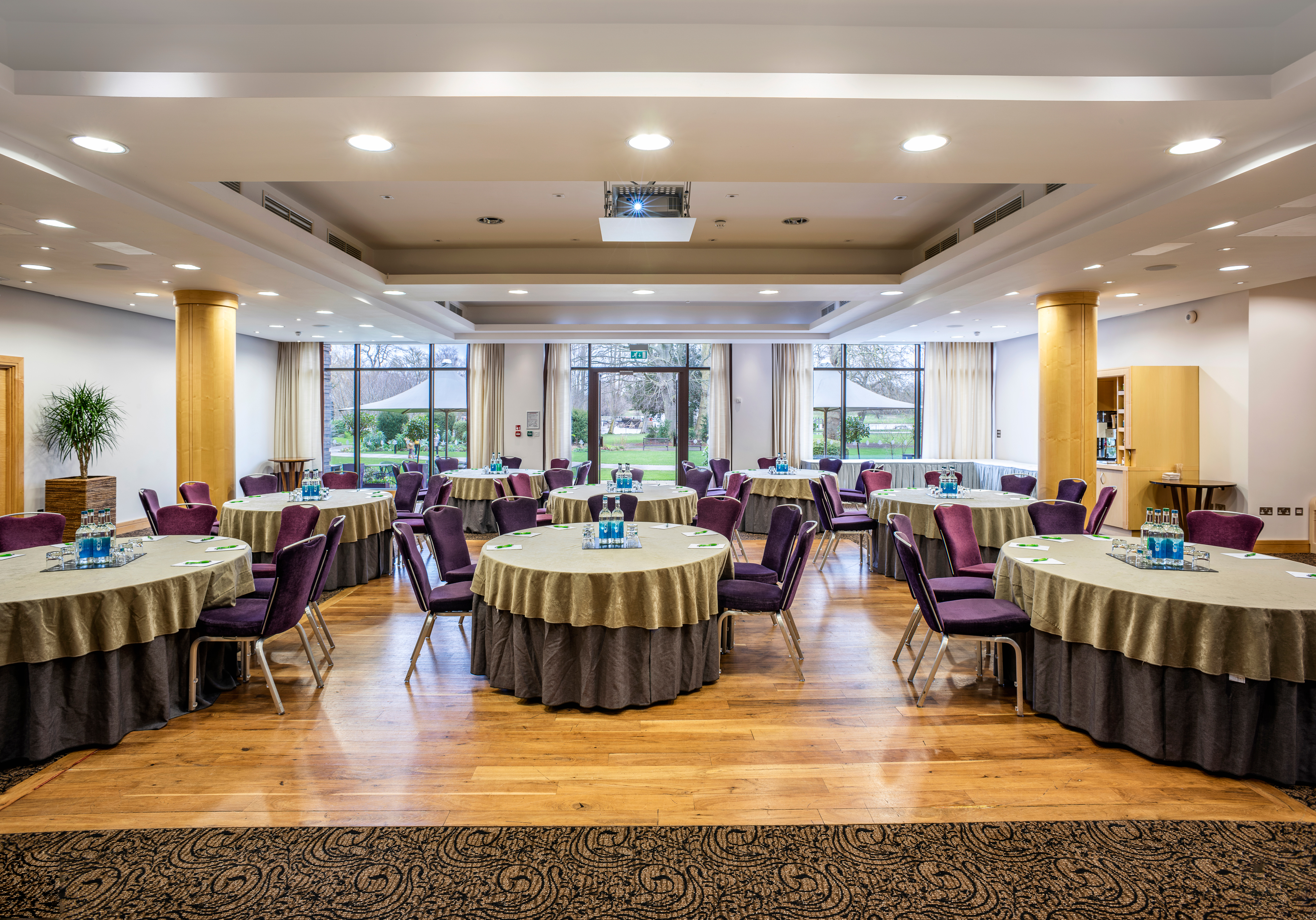 Wimbledon Room at The Lensbury: elegant meeting space with round tables and natural light.