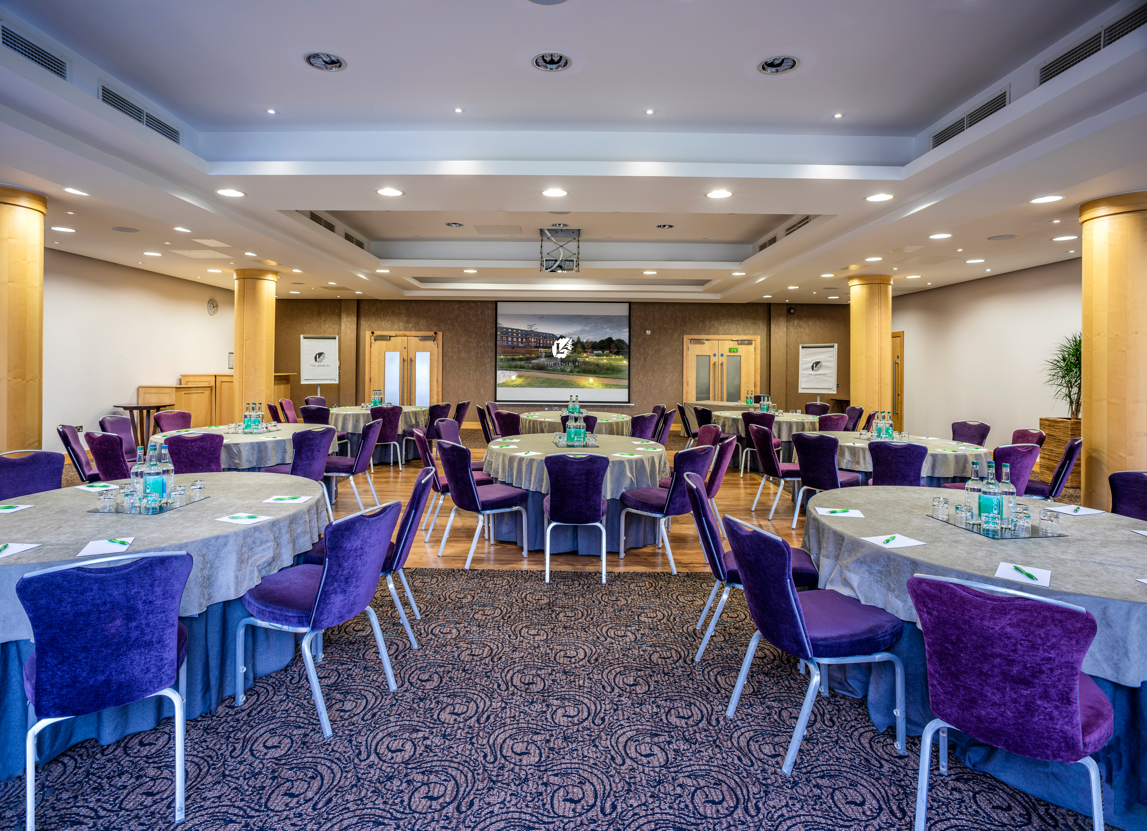 Wimbledon Room at The Lensbury with elegant gray tables and plush purple chairs for events.