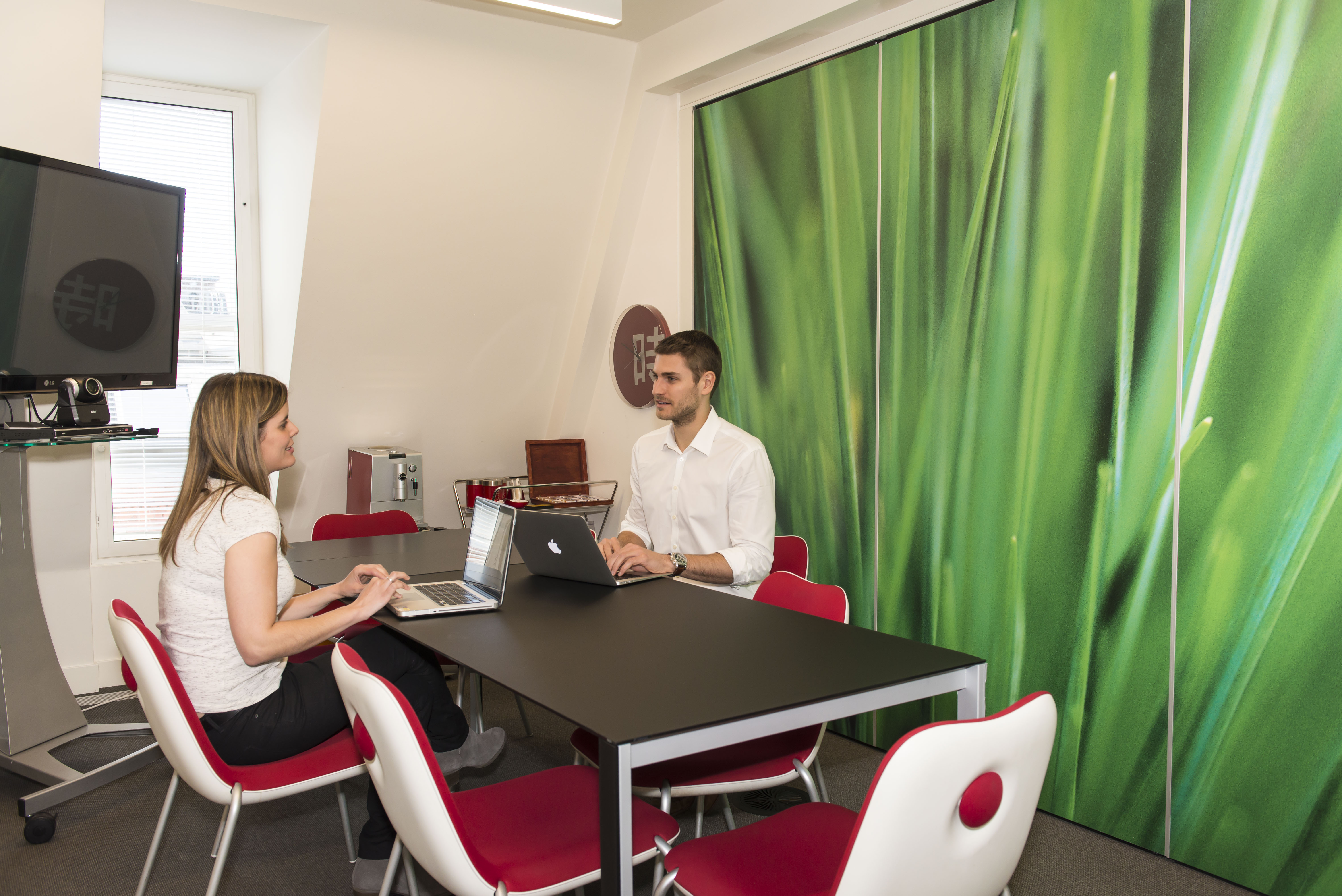 Modern video conferencing room with sleek table and vibrant green wall for team meetings.