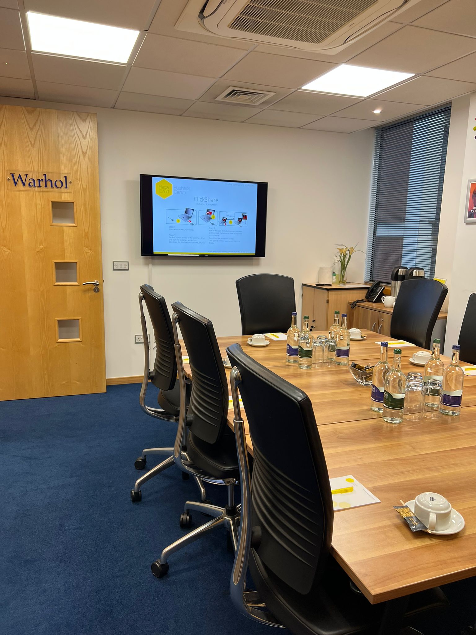 "Warhol in Regal Court meeting room with large wooden table and digital screen for discussions."