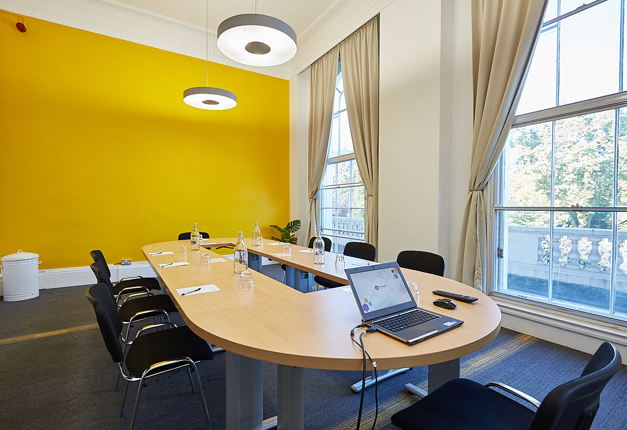 Modern meeting room with oval table and yellow accent wall for collaborative events.
