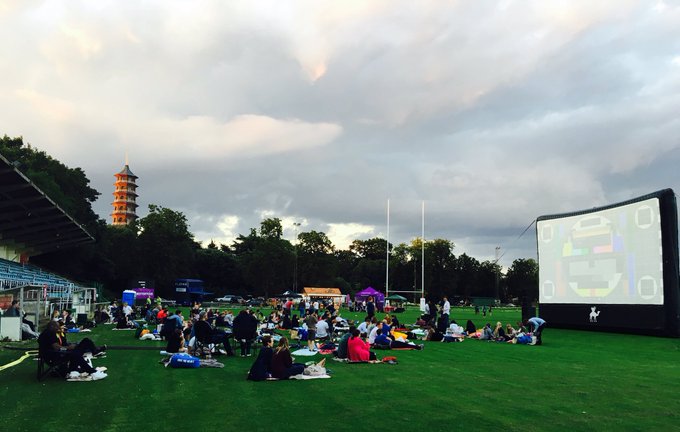 Outdoor event at Dragon's & Lion's Suites with inflatable screen and grass seating.