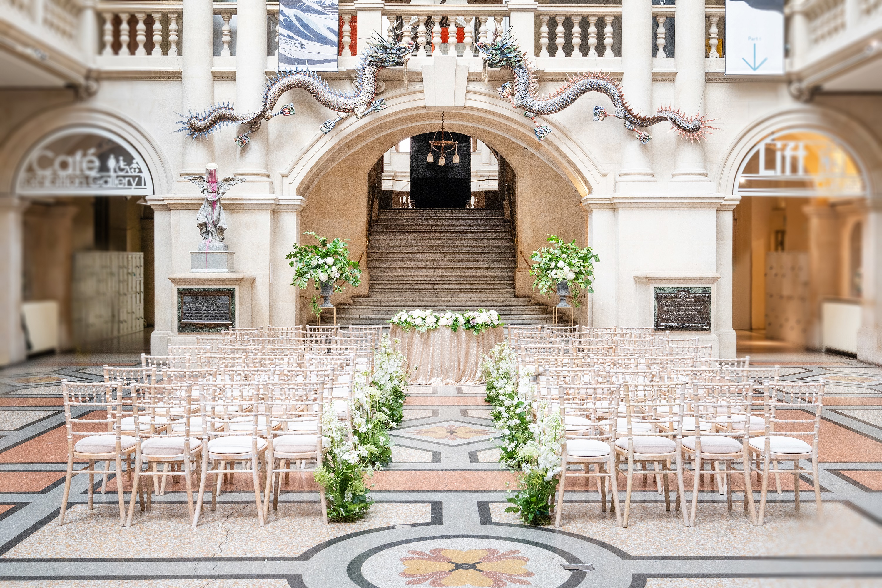 Elegant wedding setup at Bristol Museum with floral aisle and chiavari chairs.