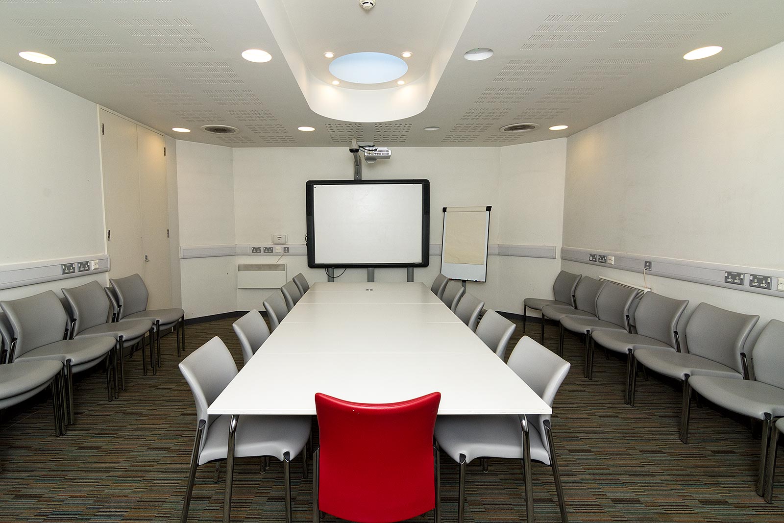 Modern library meeting room with white table, projector for collaborative events.