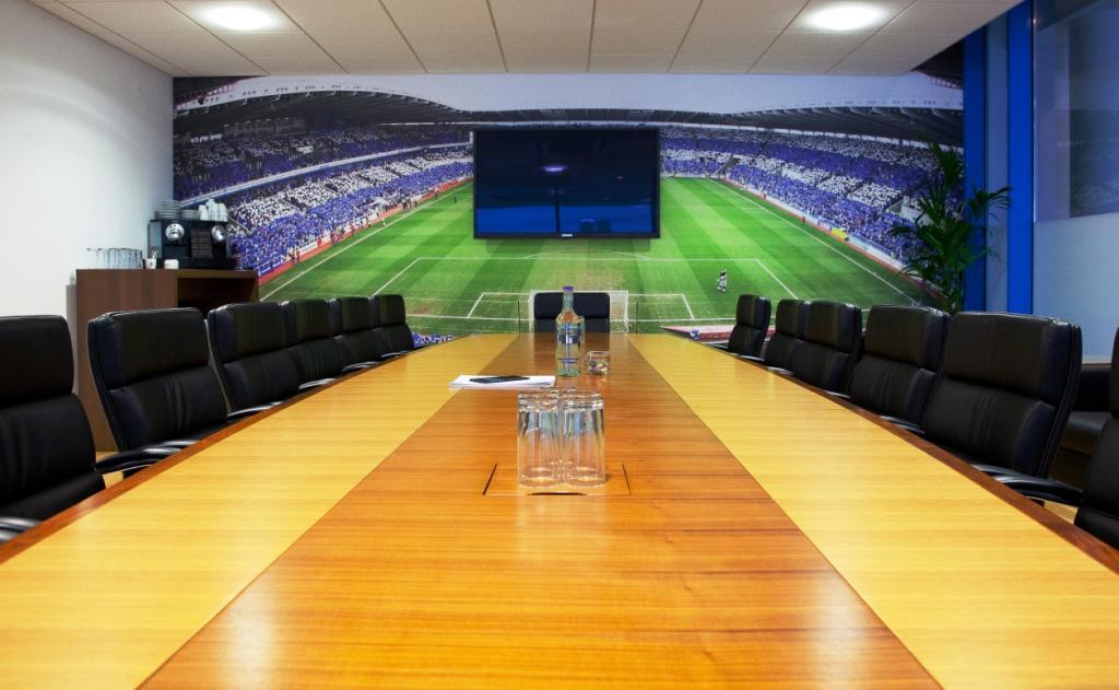 Modern conference room at Reading FC, featuring a wooden table and stadium backdrop.