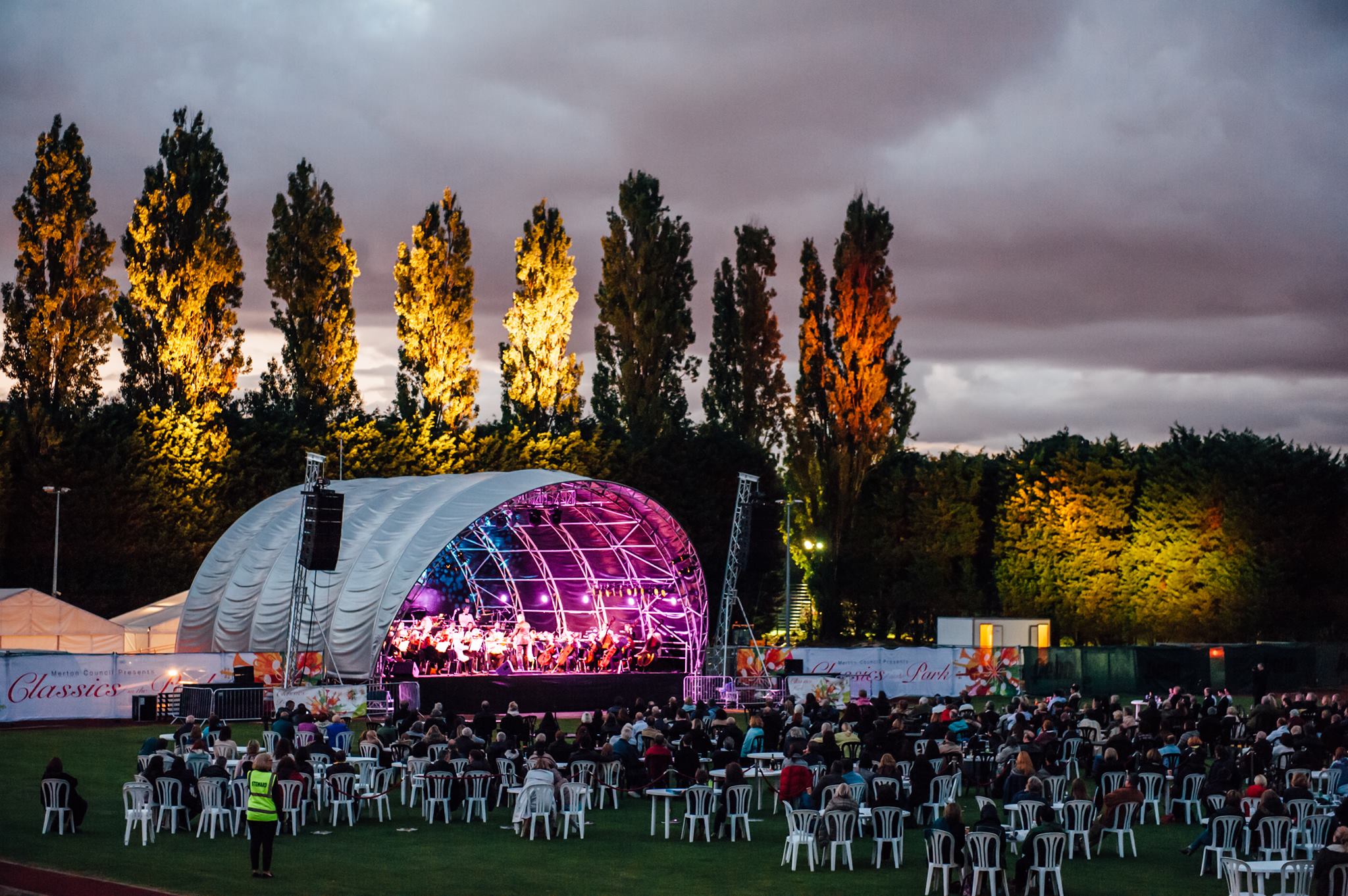 Outdoor concert setup at Wimbledon Park with vibrant stage and seated audience.