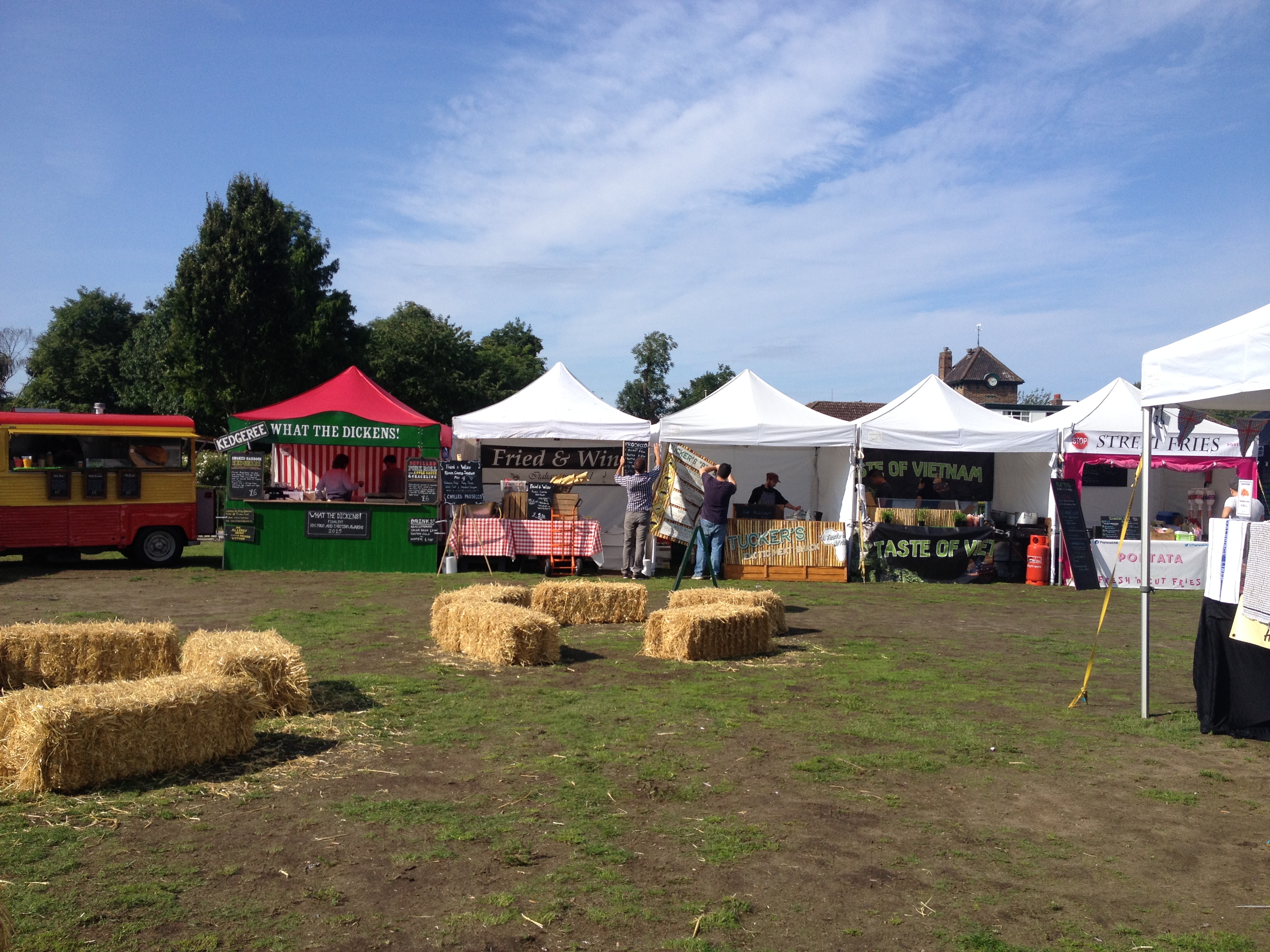 Vibrant outdoor event setup with food tents and hay bales in Wimbledon Park.