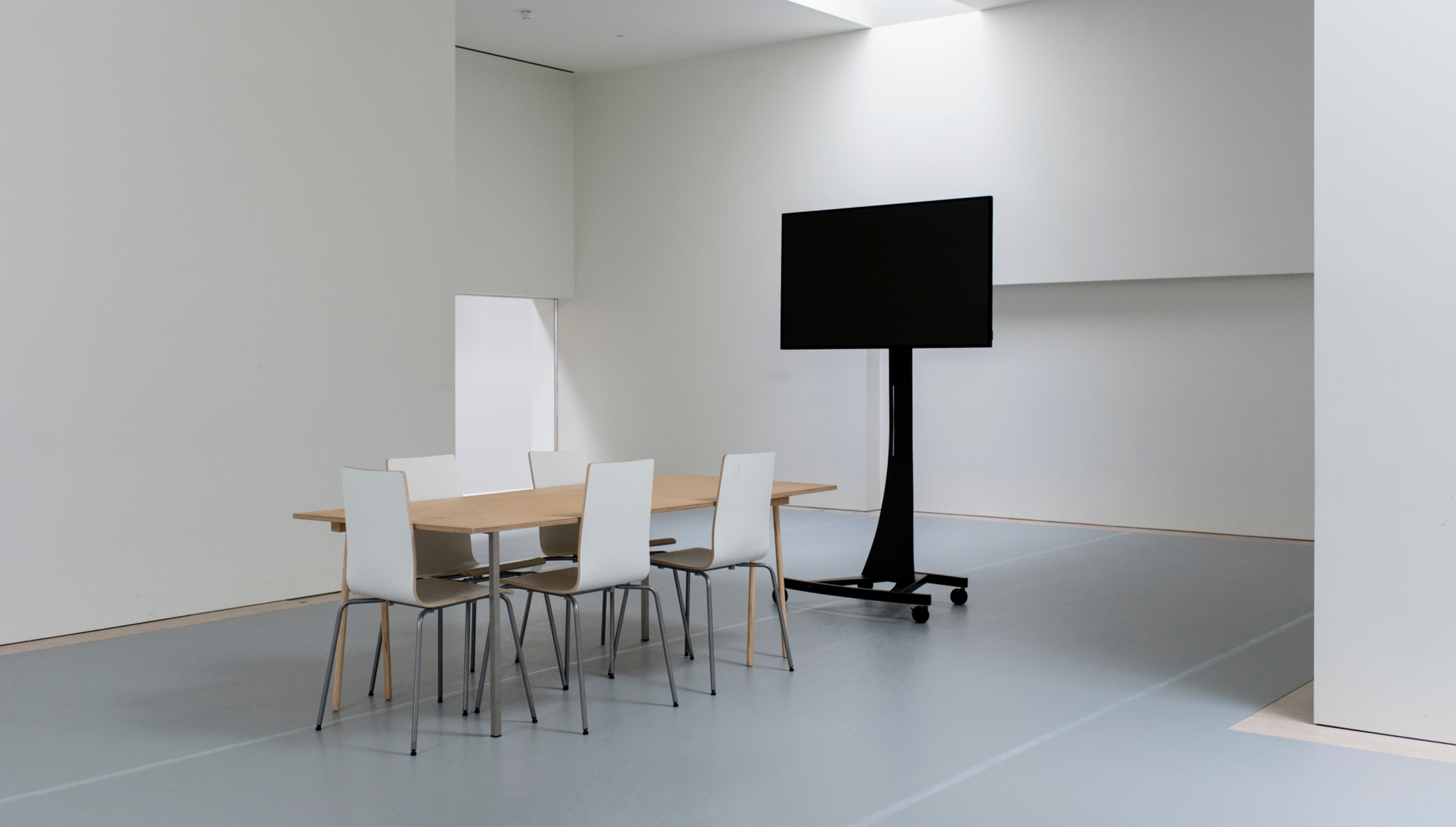 Minimalist meeting space with wooden table and white chairs, ideal for presentations.