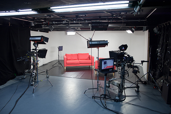 Professional TV studio with bright lighting and modern red couch for live streaming events.