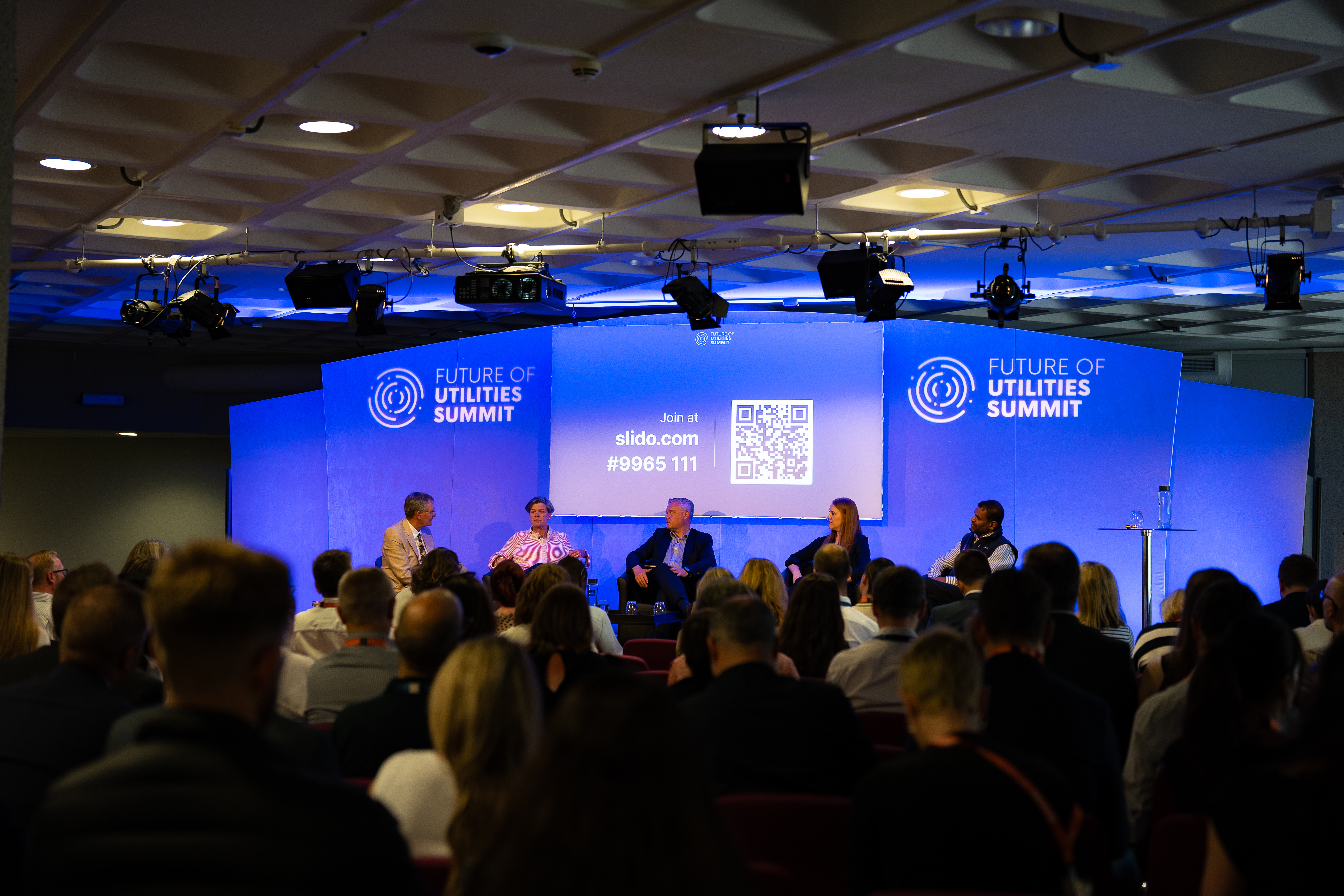 Panel discussion at Future of Utilities Summit in QEII Centre, featuring engaged audience.