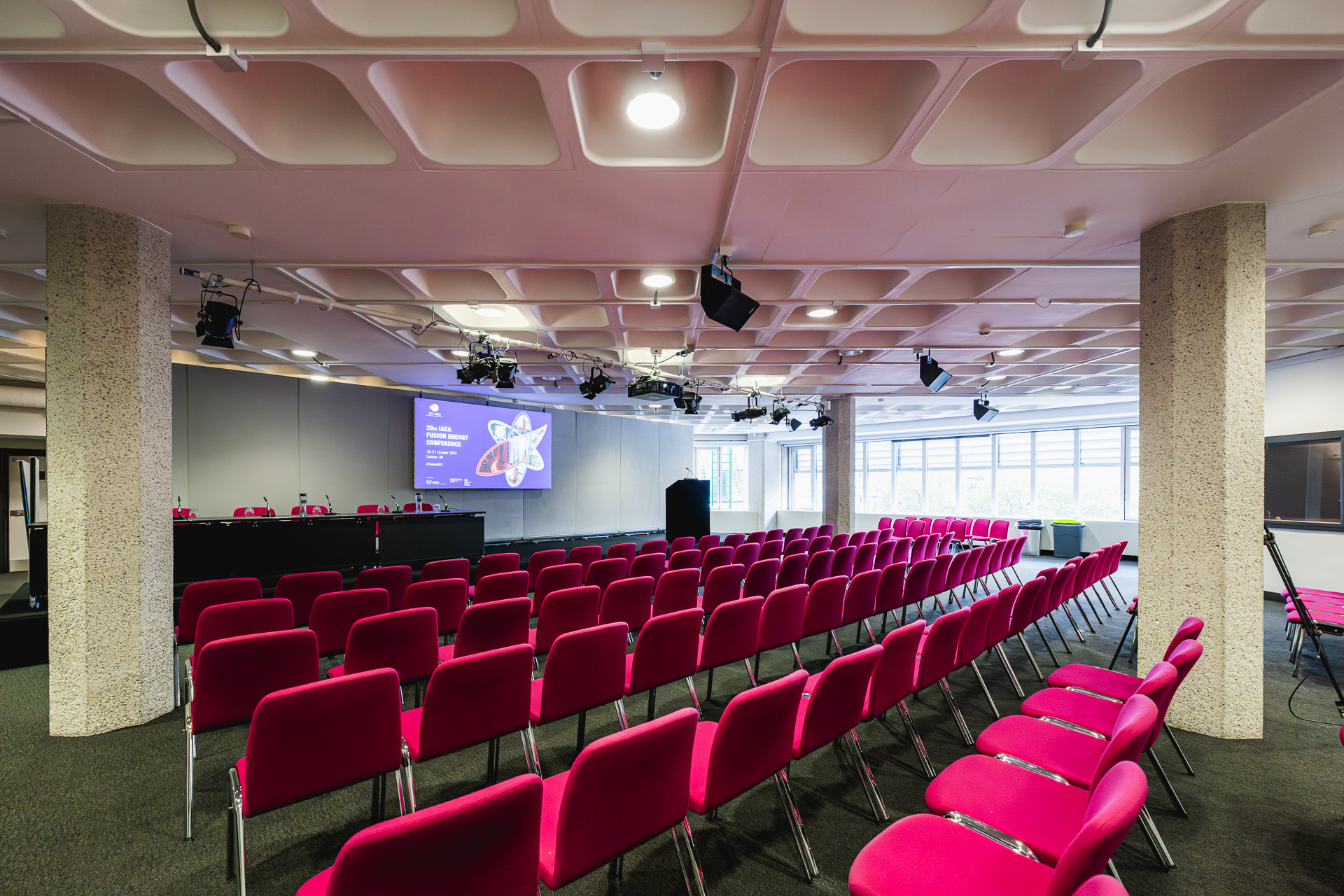 Modern conference setup in QEII Centre with vibrant pink chairs and AV technology.