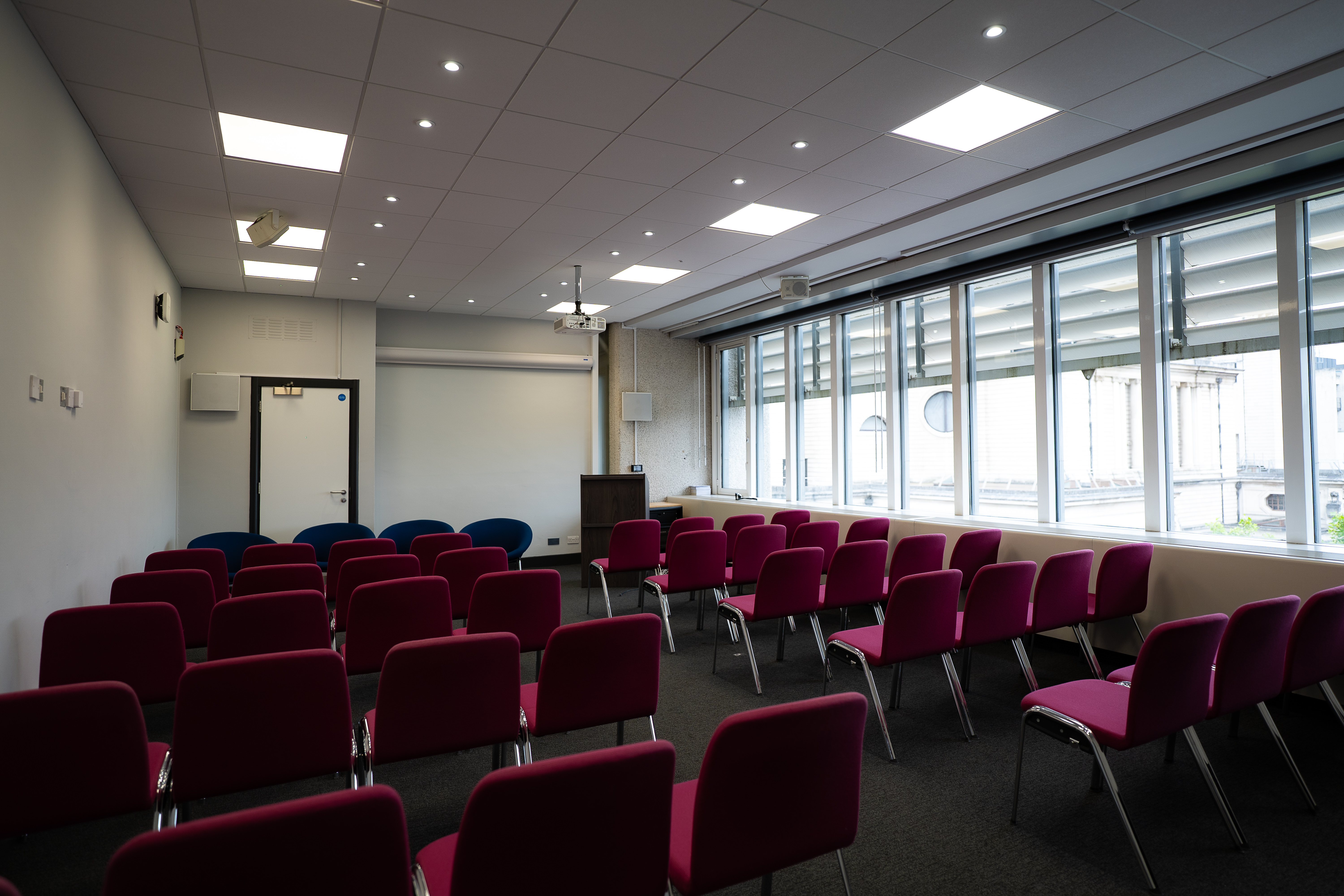 Well-lit small meeting space with pink chairs at QEII Centre for events and presentations.