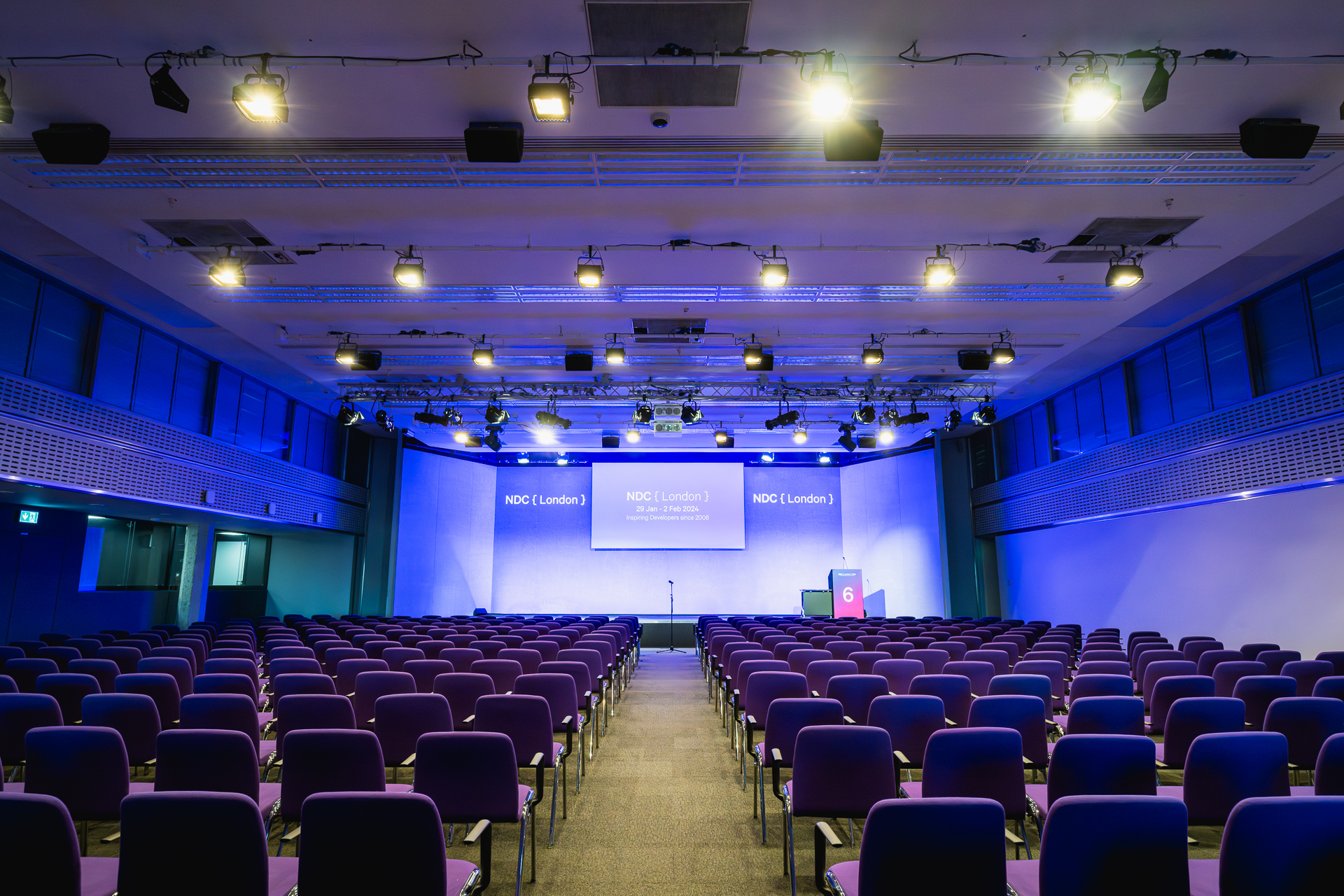 Conference space at QEII Centre with purple chairs and blue-lit stage for impactful events.