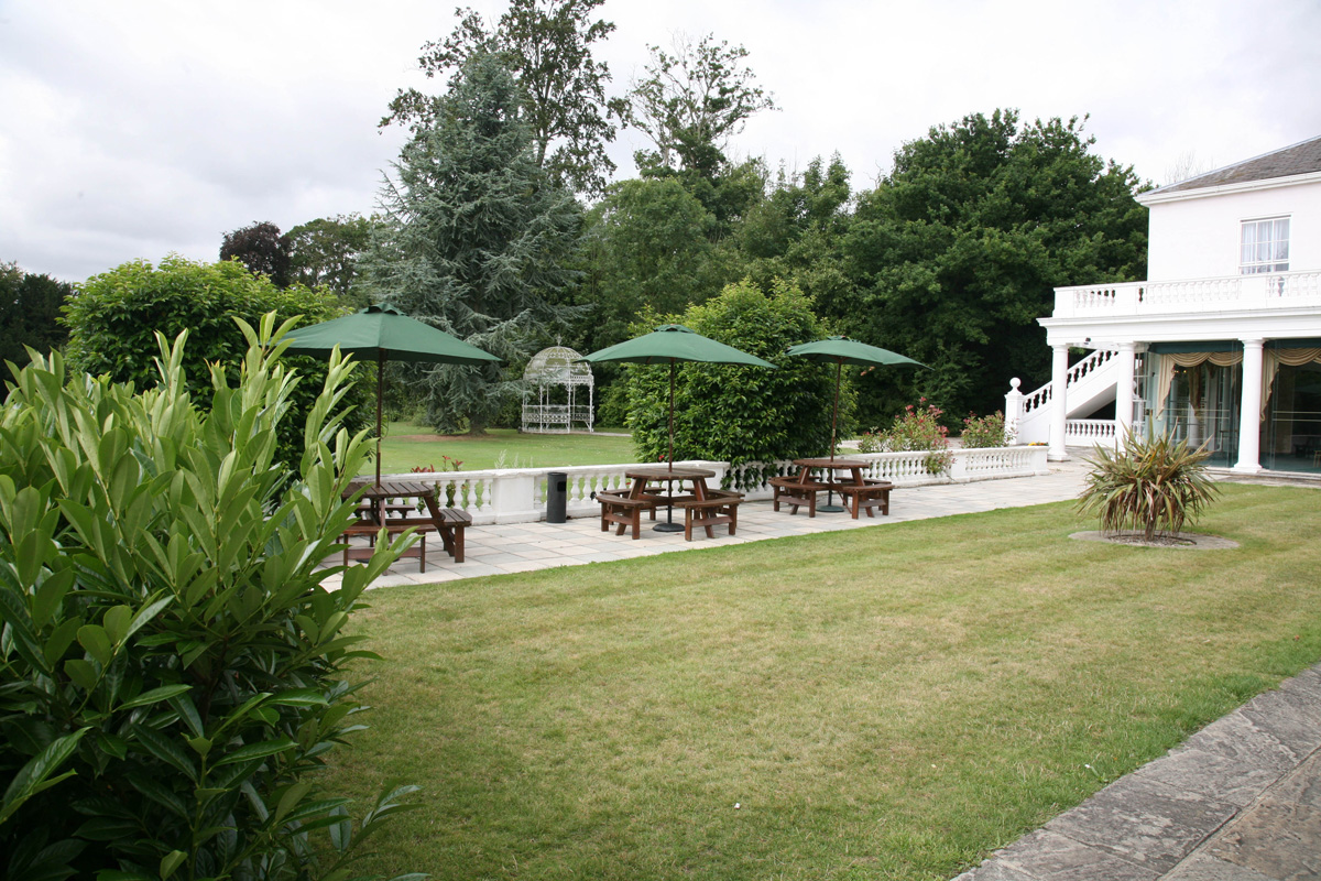 Outdoor event space at Manor of Groves Hotel with seating under green umbrellas.