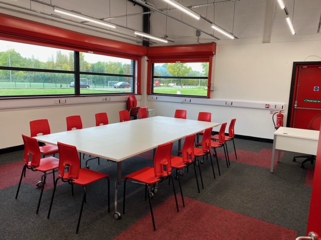Modern meeting room with large table and red chairs for workshops at FC United of Manchester.